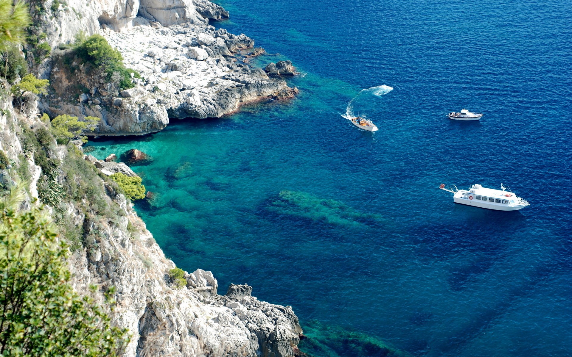 Boats near a rocky coastline with clear blue water HD Wallpaper
