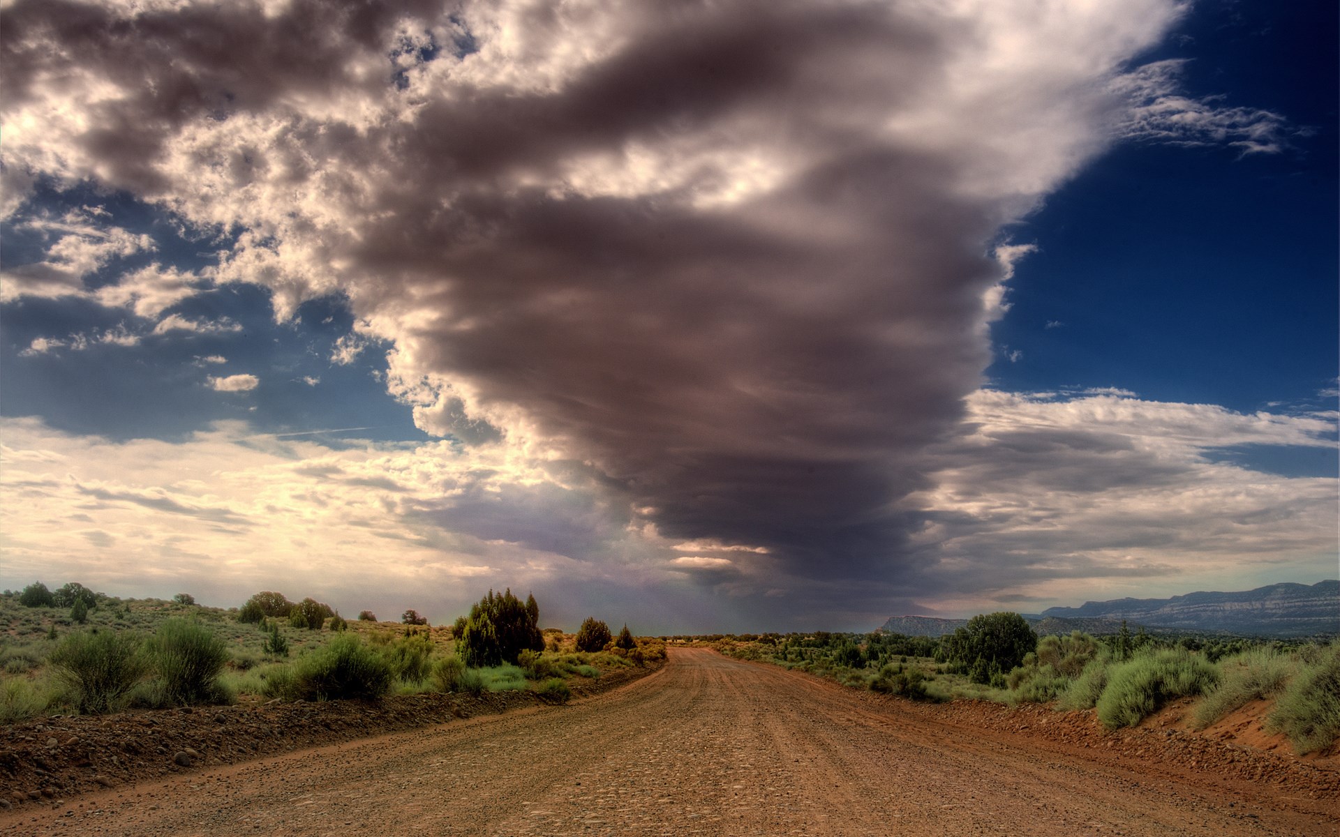 Dirt road through a desert landscape under dramatic clouds HD Wallpaper