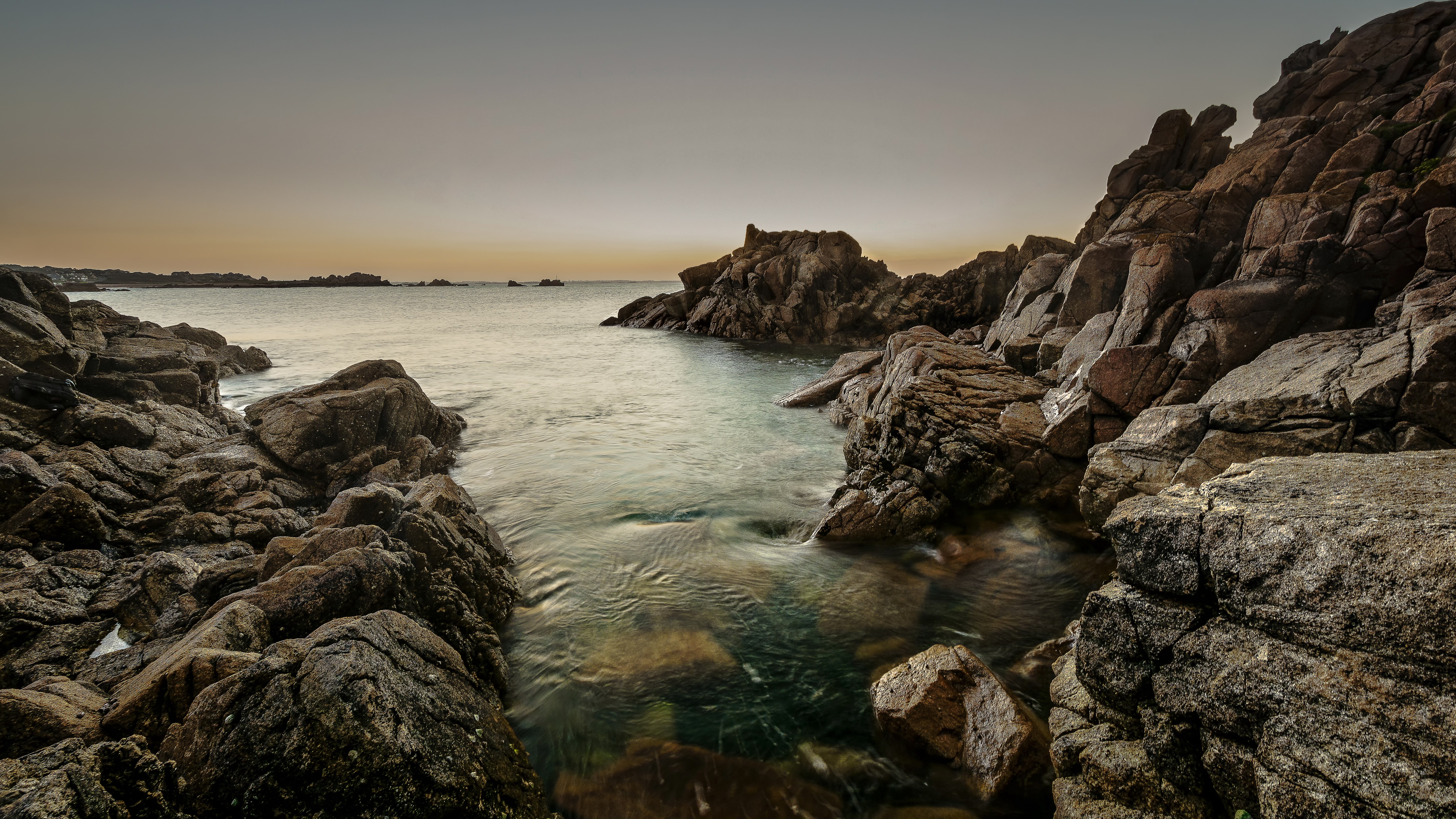 Rocky coastline with calm ocean at dusk HD Wallpaper