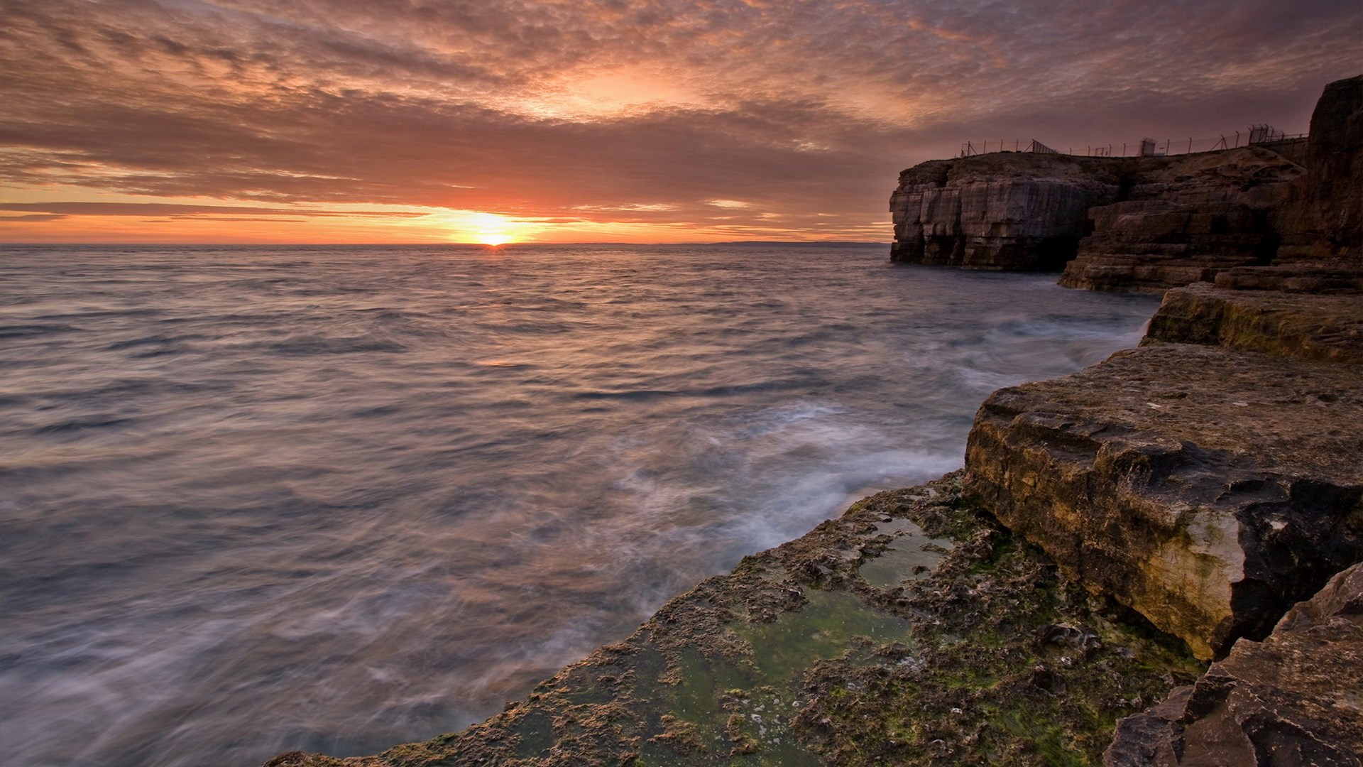 Sunset over the ocean with rocky cliffs HD Wallpaper