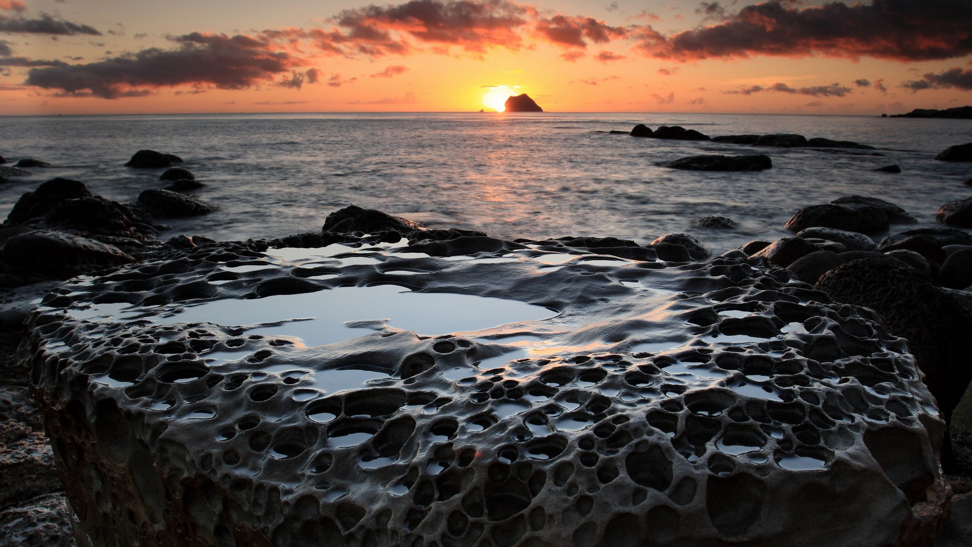 Rocky coastline at sunset with island in distance HD Wallpaper