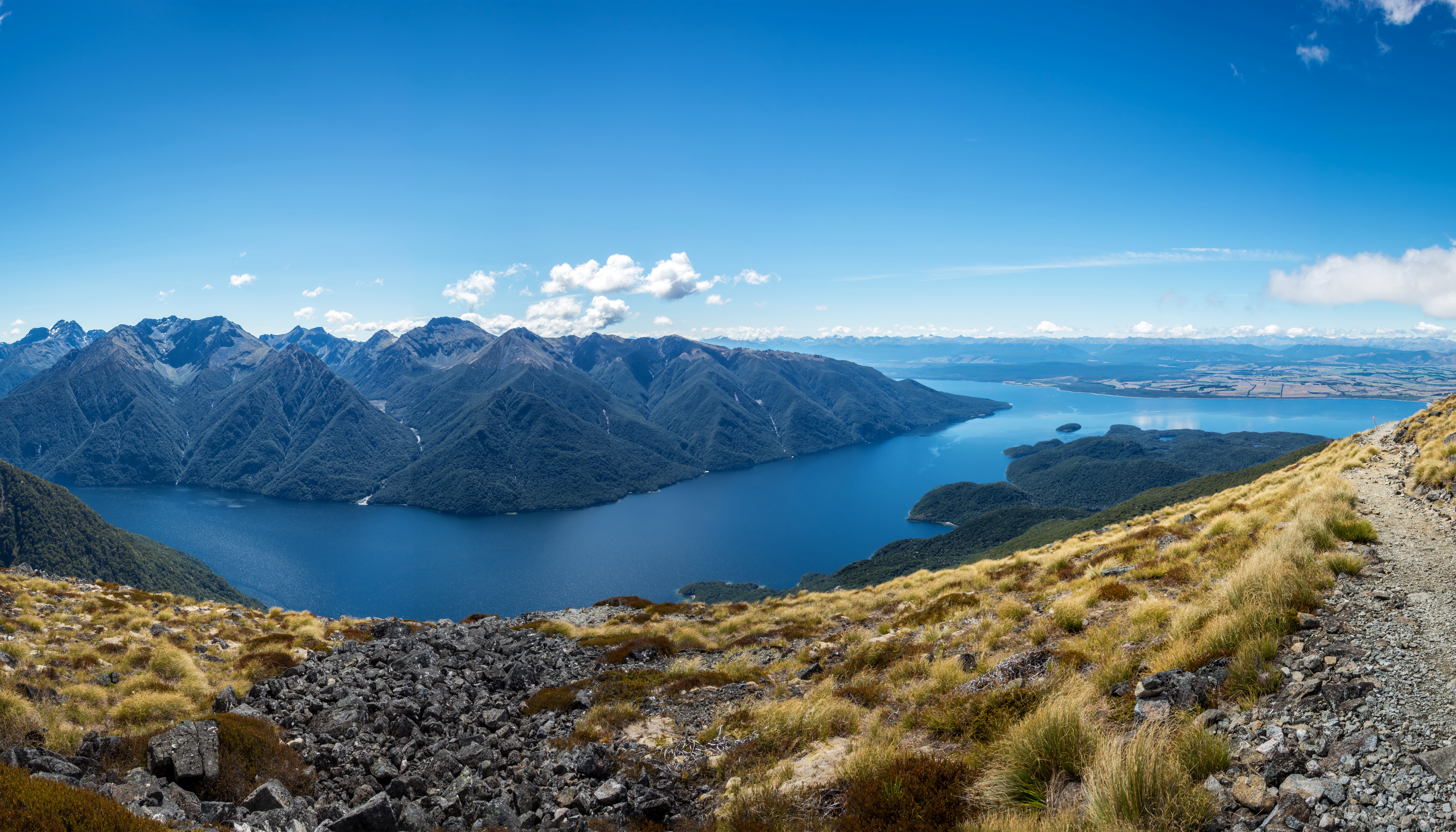 Panoramic view of mountains and lake under a blue sky HD Wallpaper