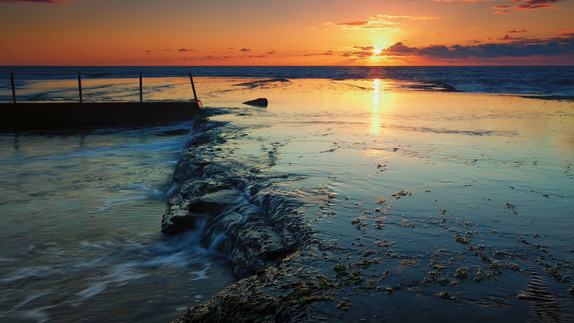 Sunset over ocean with rock pool and wooden posts HD Wallpaper