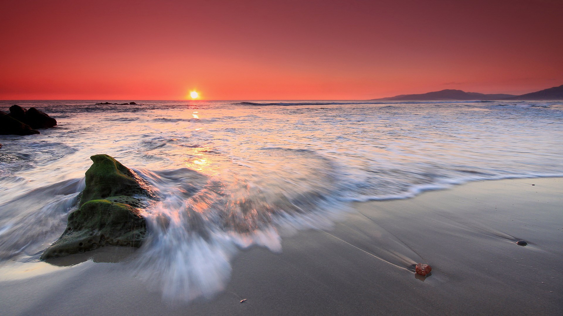 Sunset over the ocean with waves crashing on a rocky beach HD Wallpaper