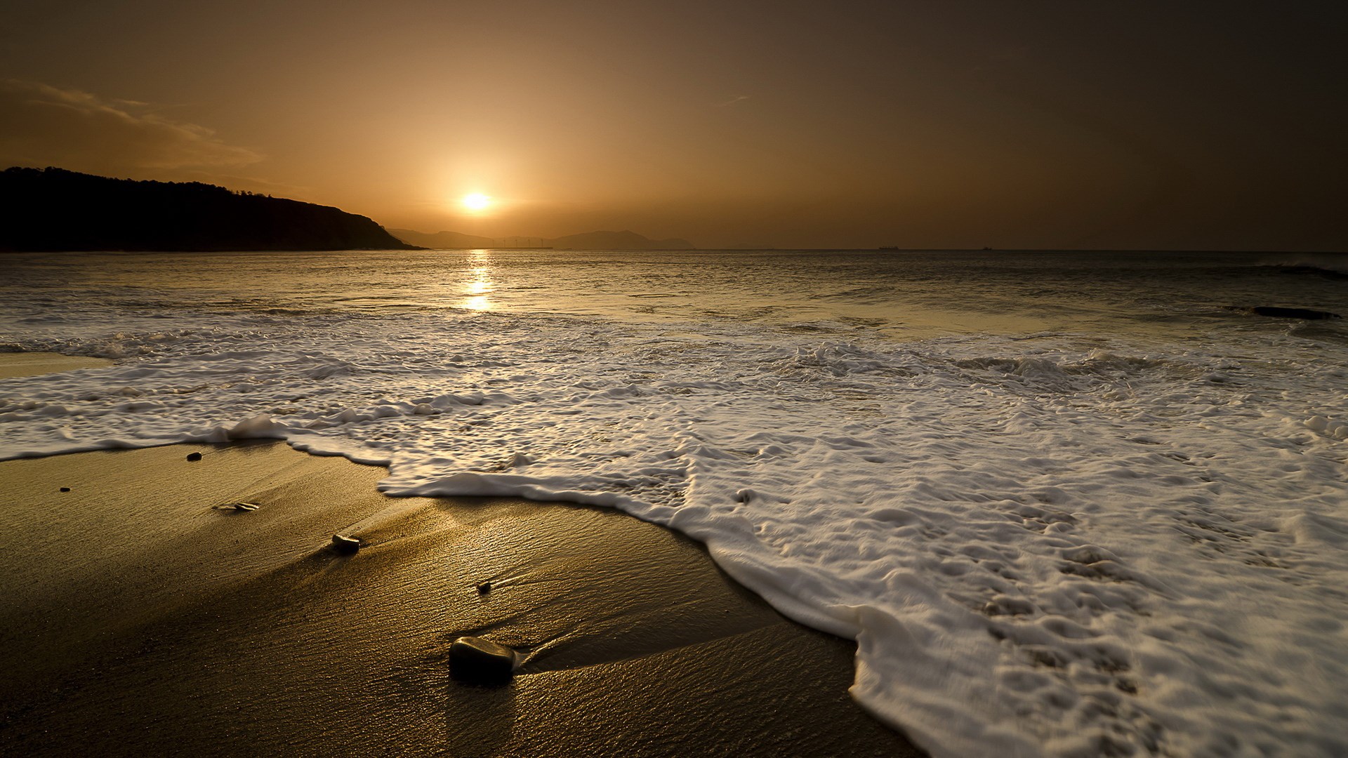 Sunset over the ocean with waves crashing on the beach HD Wallpaper