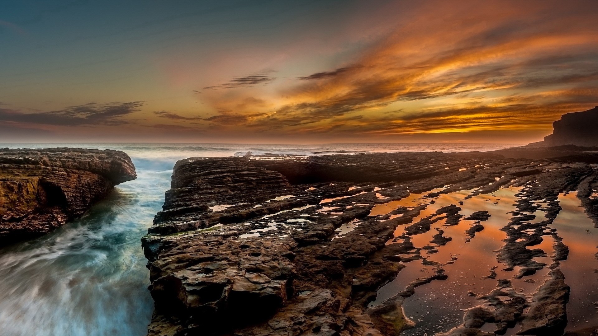 Rocky coastline at sunset with ocean waves HD Wallpaper