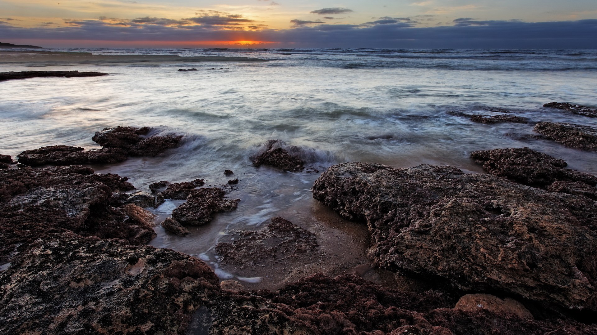 Rocky coastline at sunset with waves HD Wallpaper