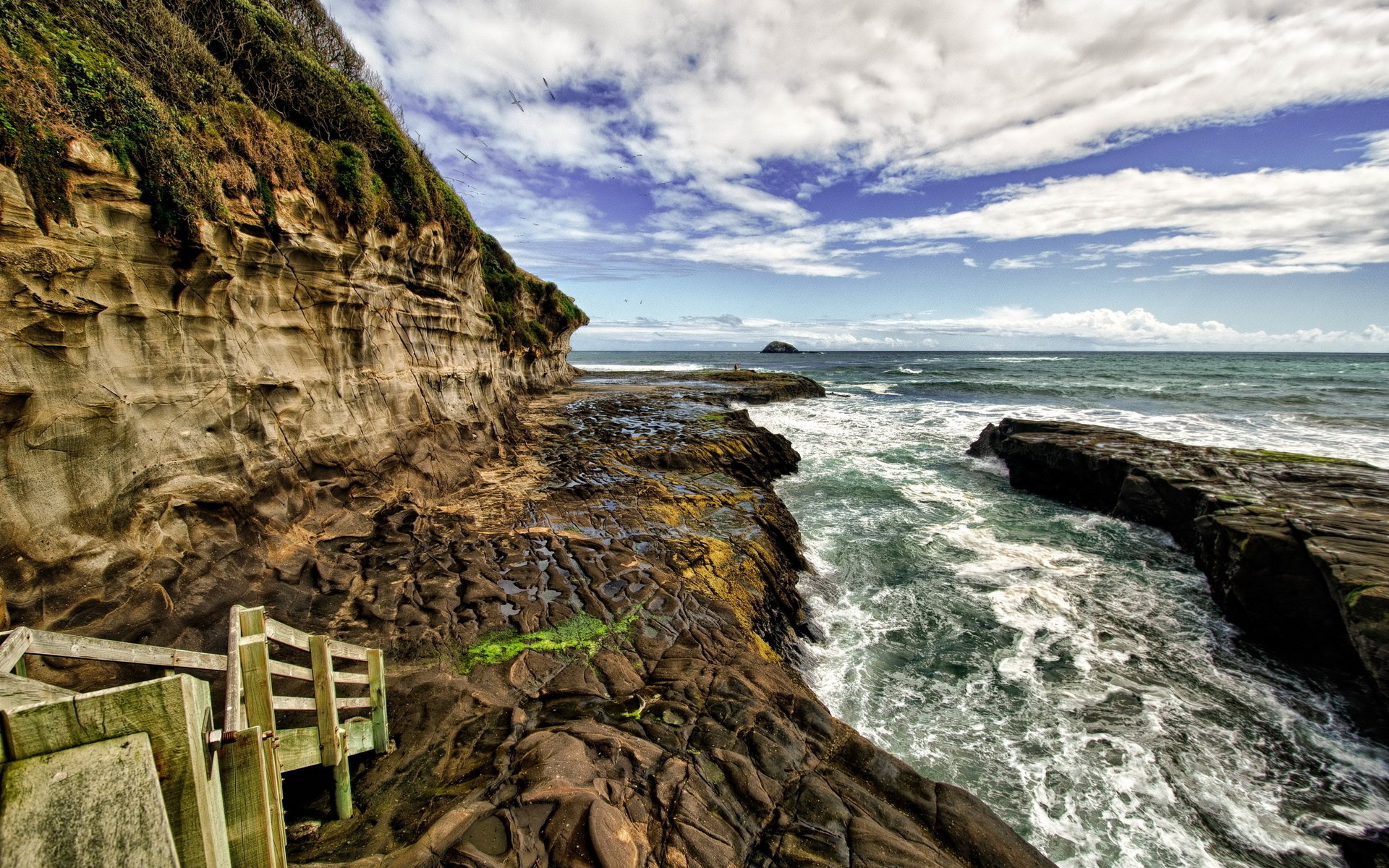 Wooden stairs leading to a rocky coastline with waves HD Wallpaper