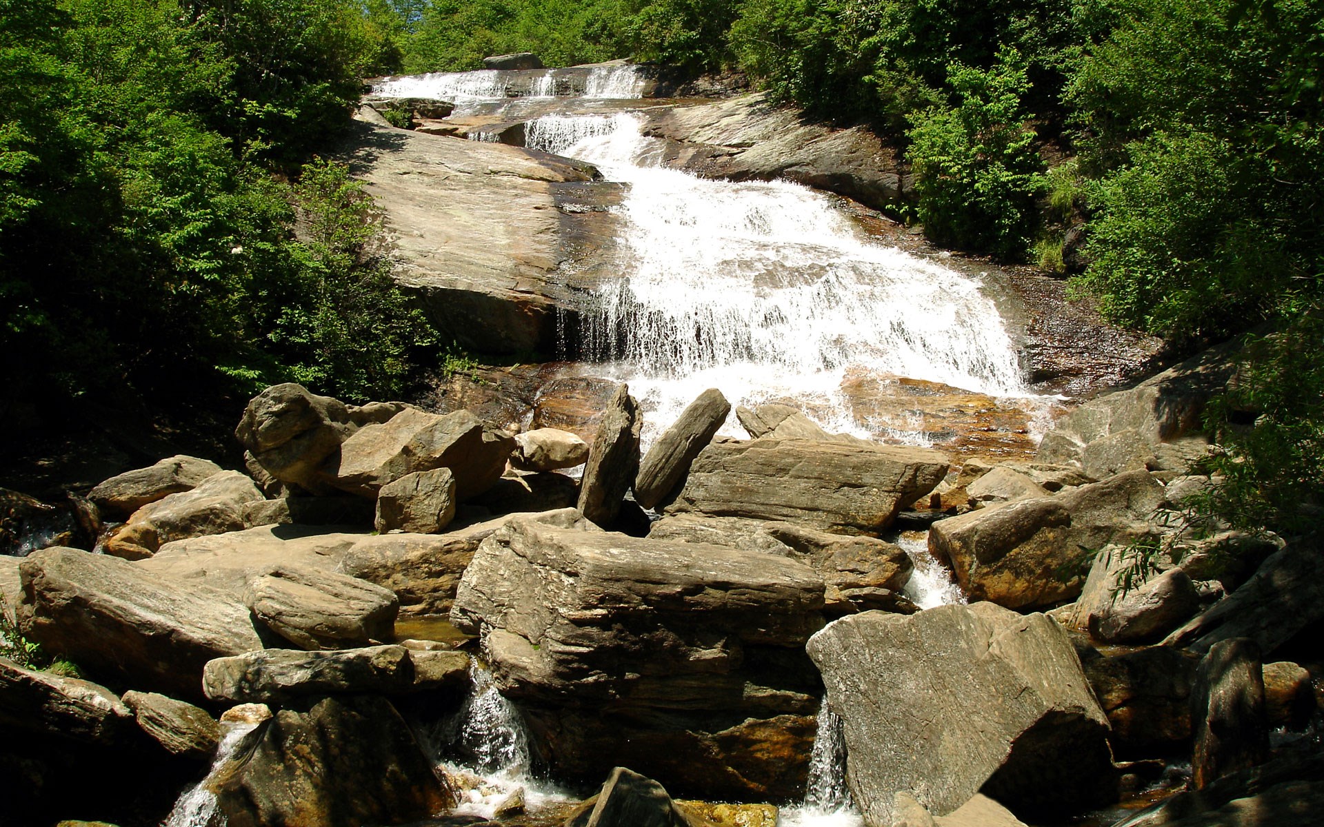 Waterfall cascading over rocks with green trees HD Wallpaper