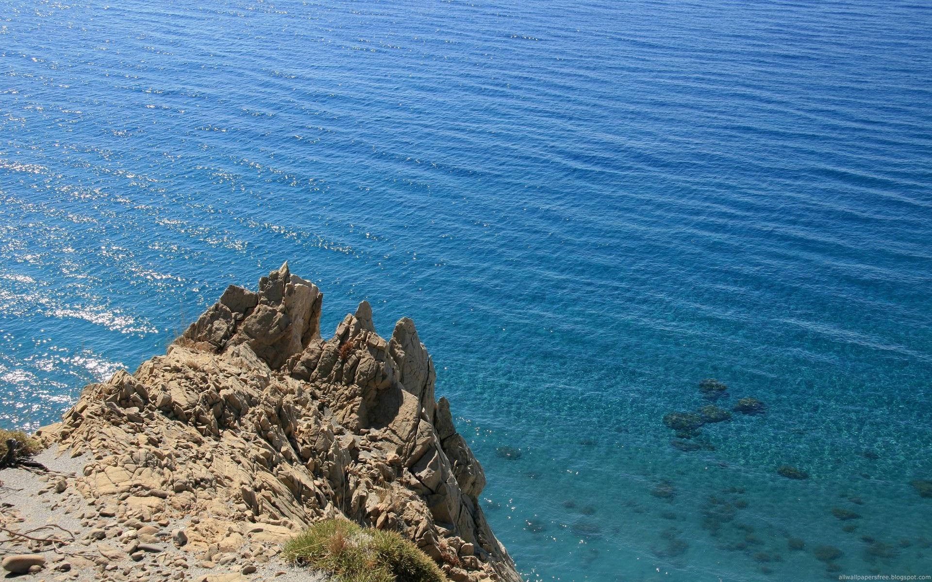 Rocky cliff overlooking a clear blue ocean HD Wallpaper