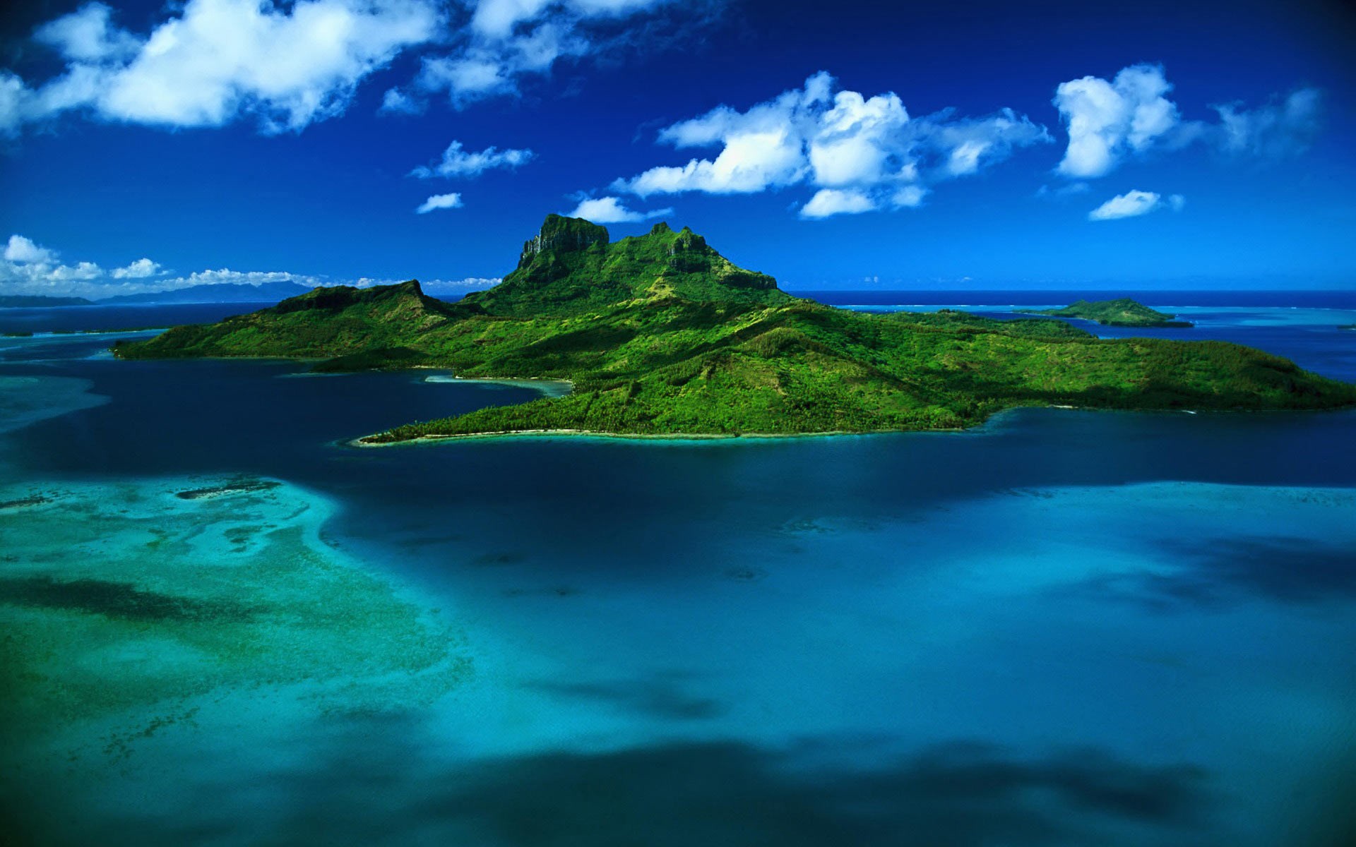 Aerial view of a tropical island with lush green mountains surrounded by turquoise water HD Wallpaper