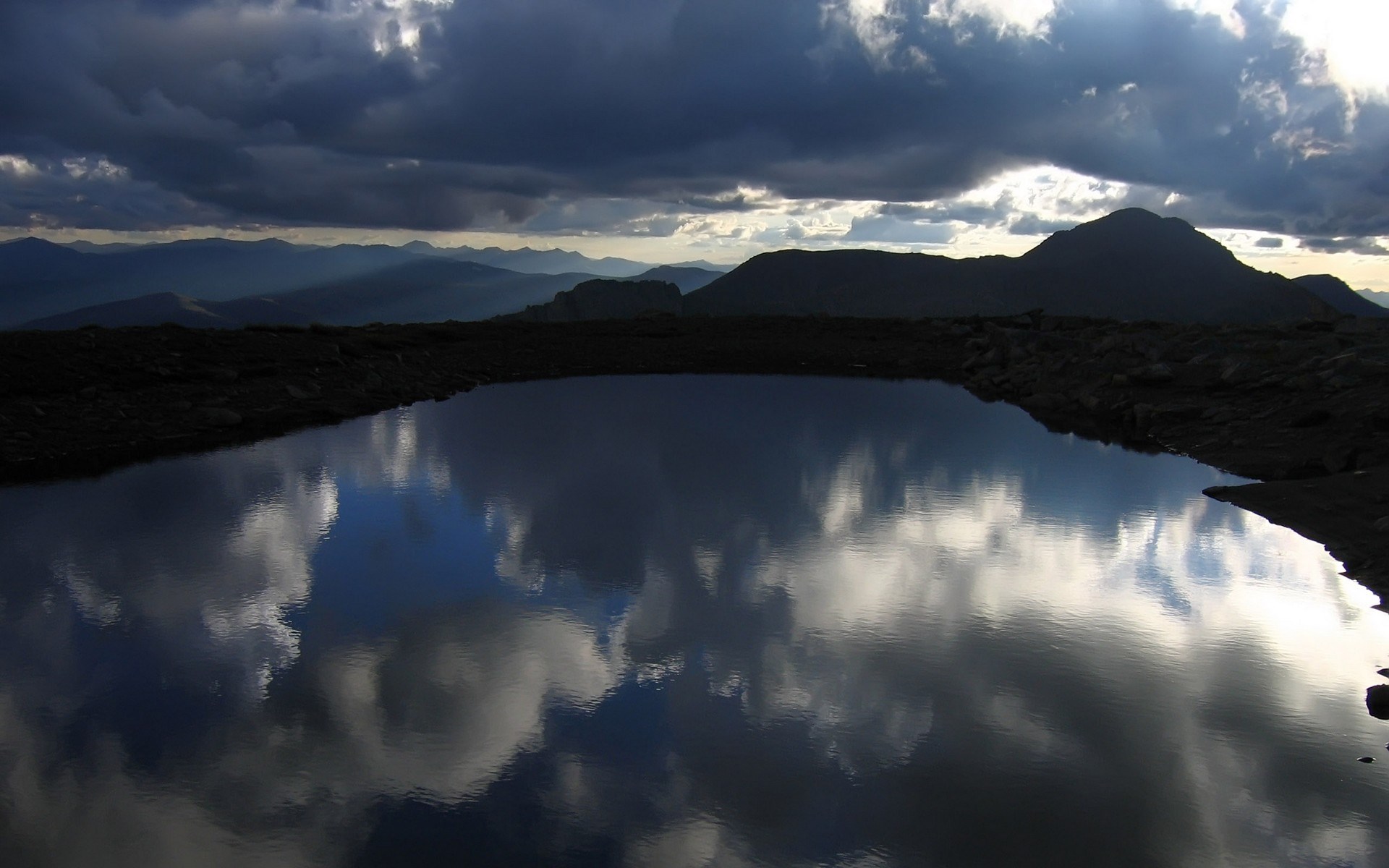 Mountain lake reflecting stormy clouds and distant peaks HD Wallpaper