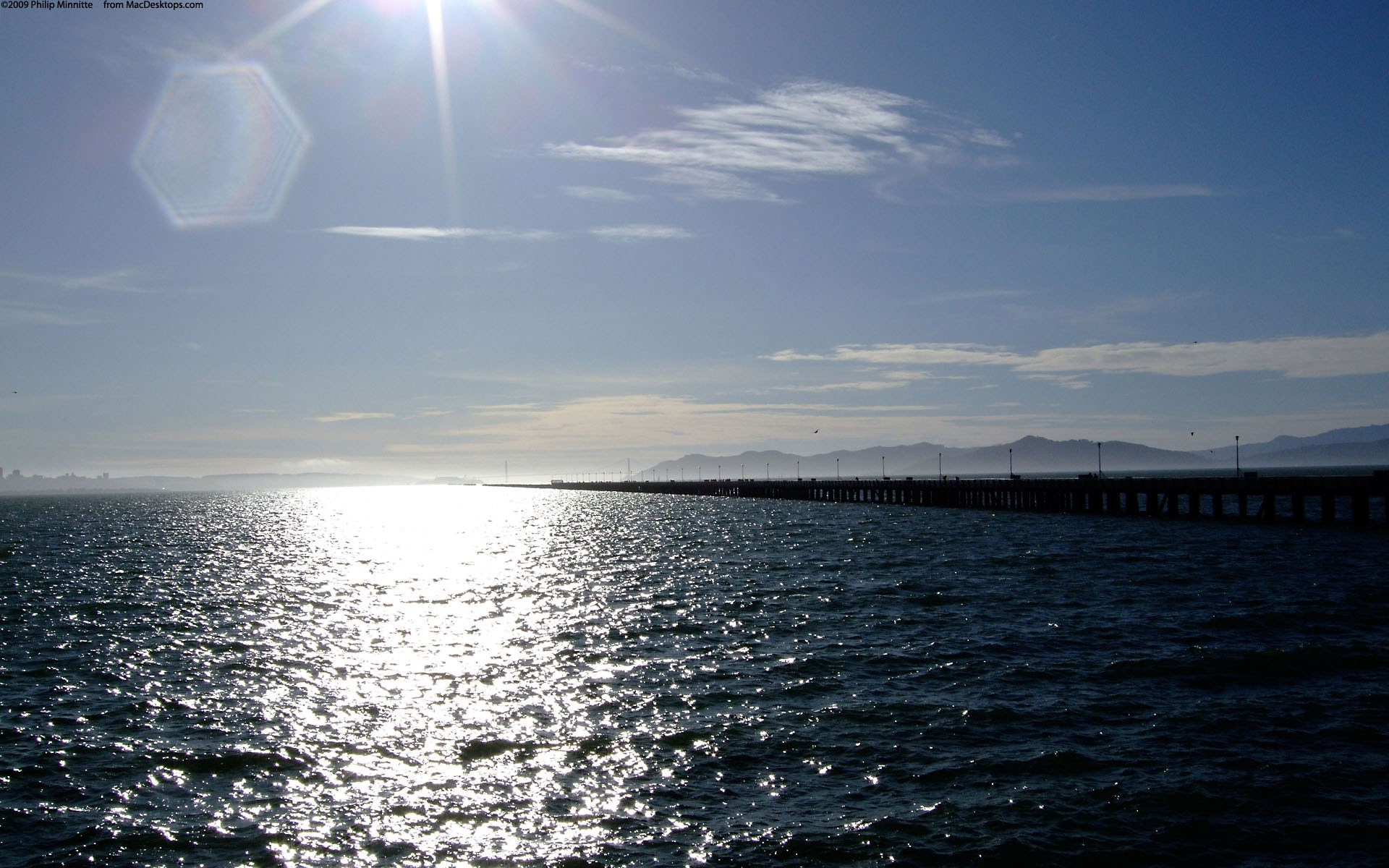 Pier extending into the ocean with sun glare HD Wallpaper