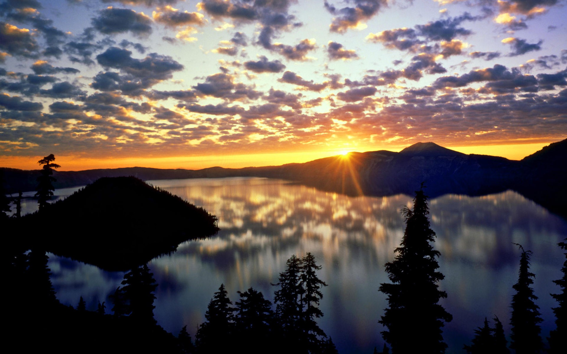 Sunset over a calm lake with silhouetted trees and mountains HD Wallpaper