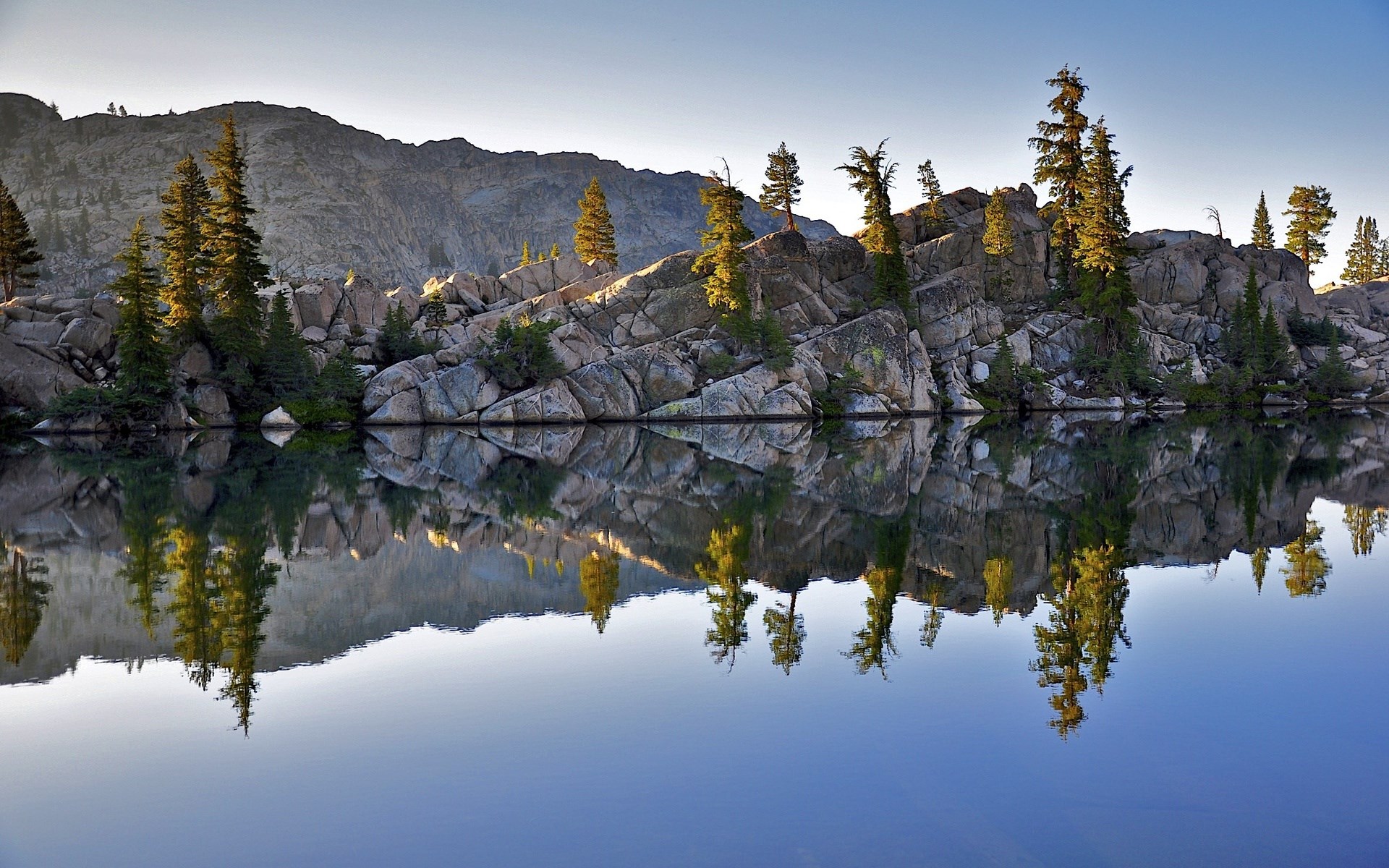 Lake reflection of rocky shore with pine trees HD Wallpaper
