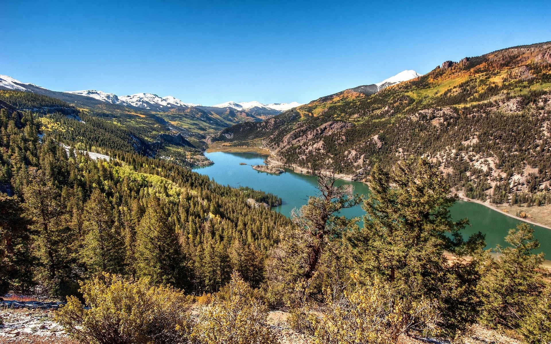 Mountain lake surrounded by pine forest and snow-capped peaks HD Wallpaper