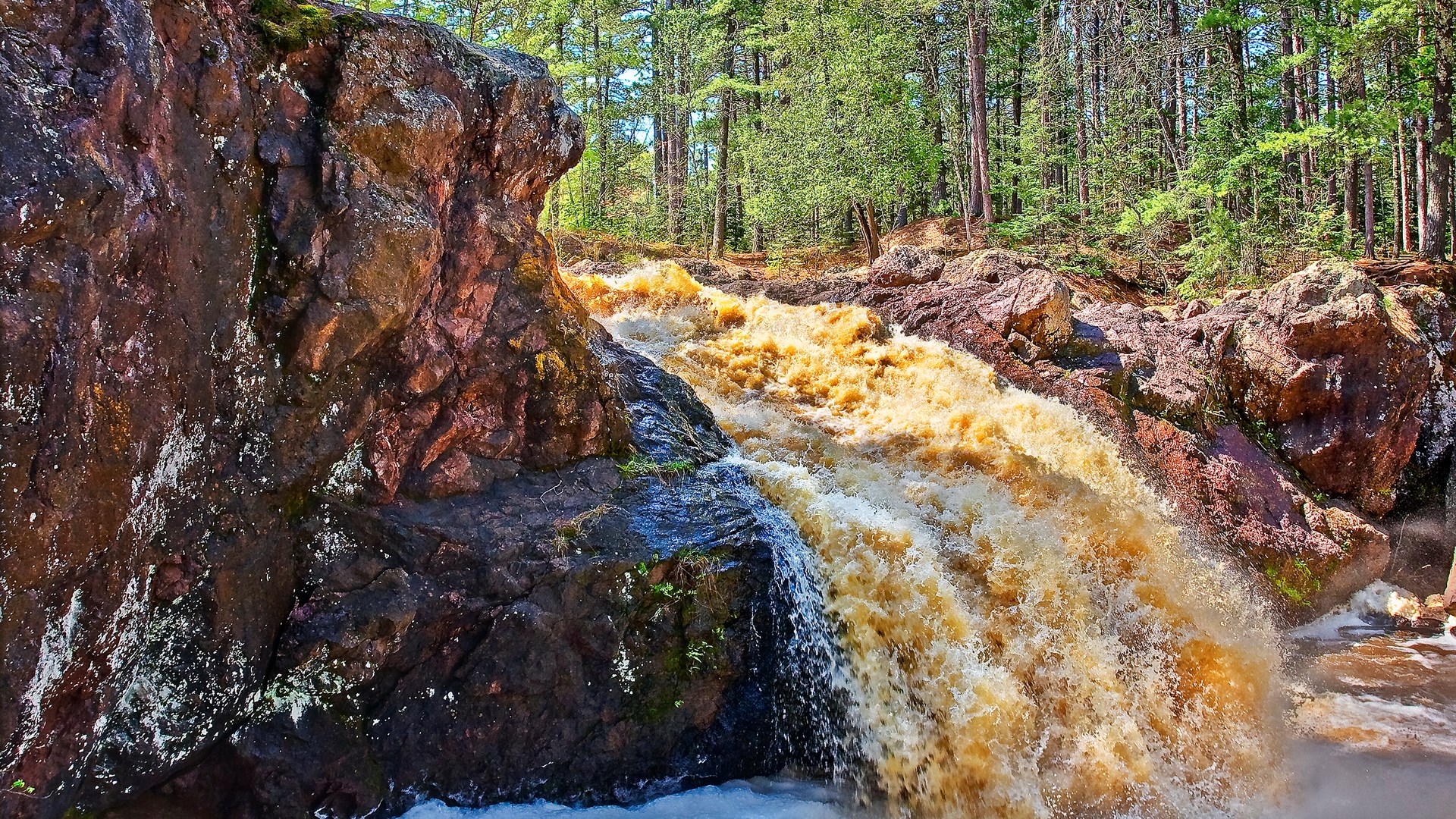 Brown waterfall cascading over rocks in a forest HD Wallpaper