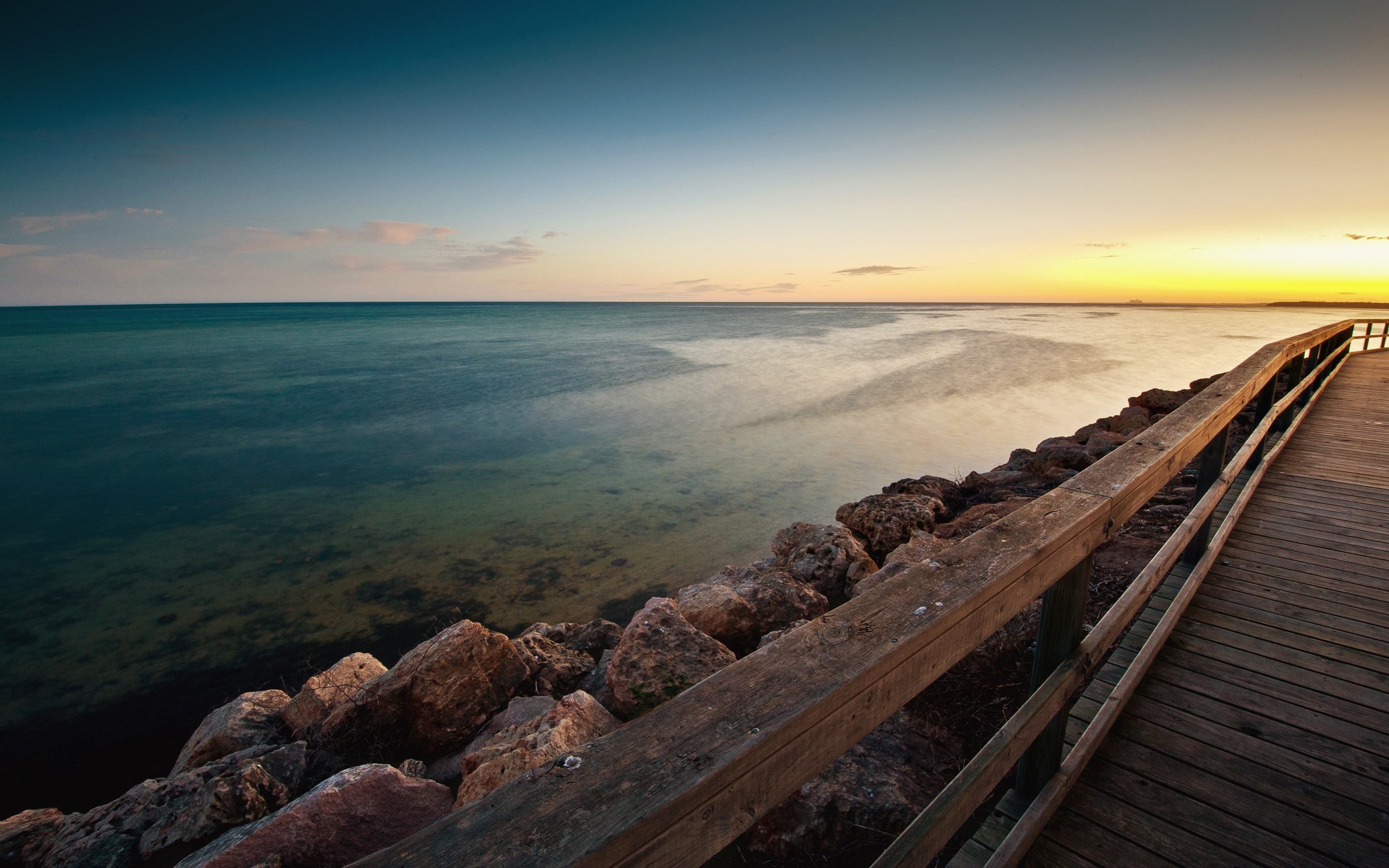 Wooden pier along a rocky coastline at sunset HD Wallpaper