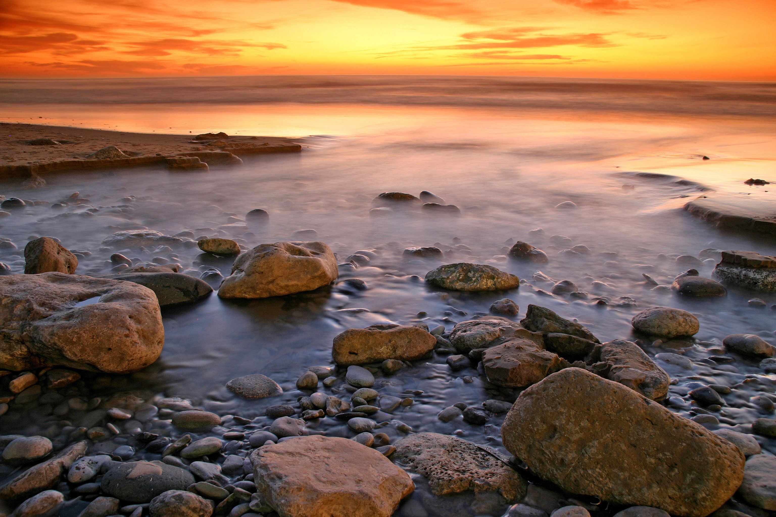 Rocky beach at sunset with orange sky HD Wallpaper