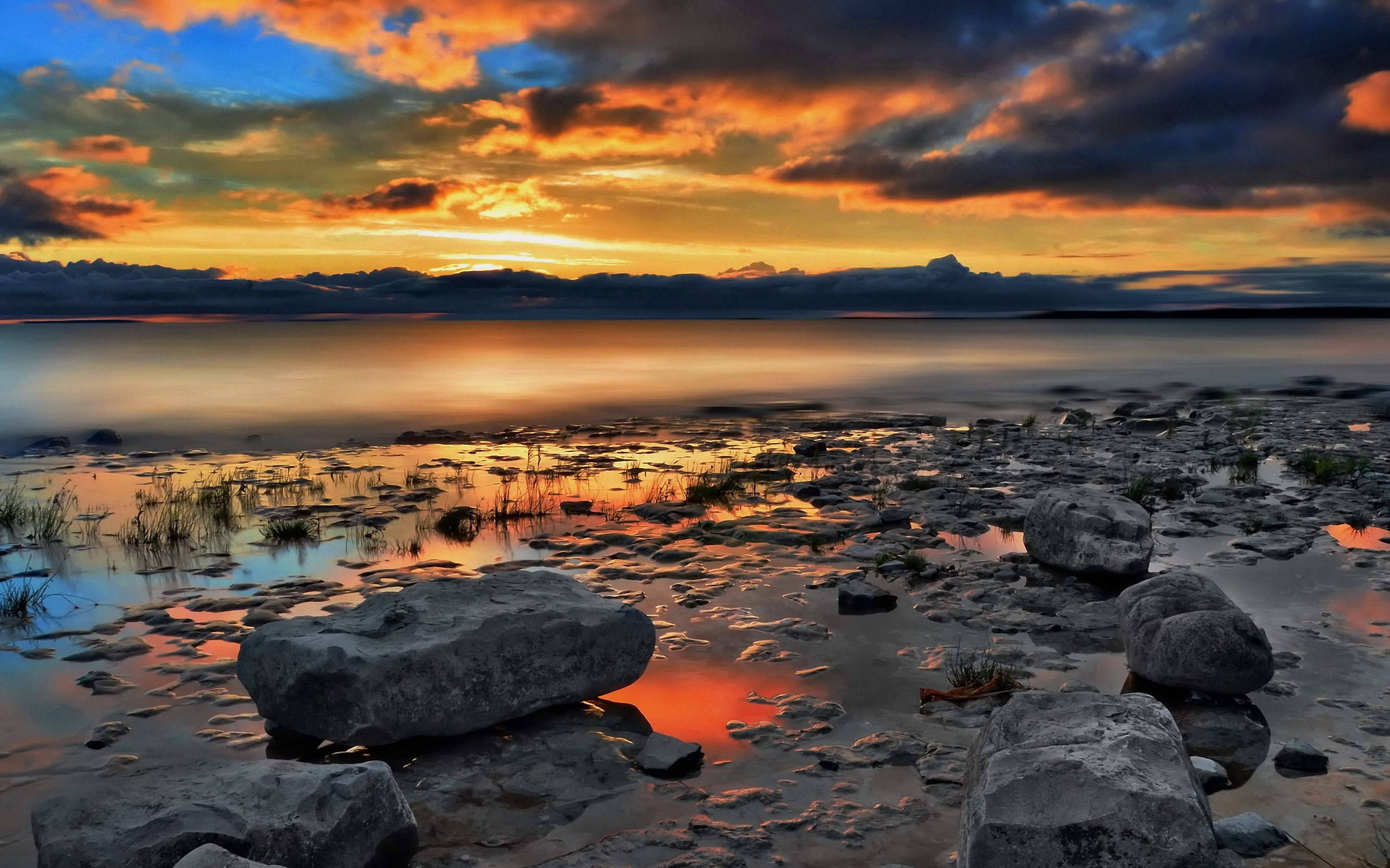 Sunset over a rocky shore with calm water HD Wallpaper