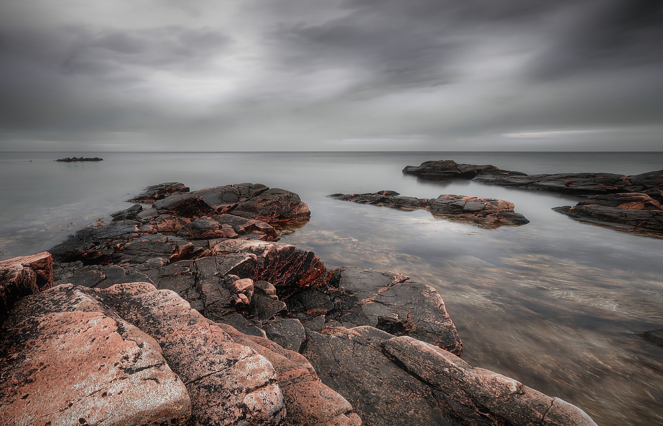 Rocky coastline with calm water under cloudy sky HD Wallpaper