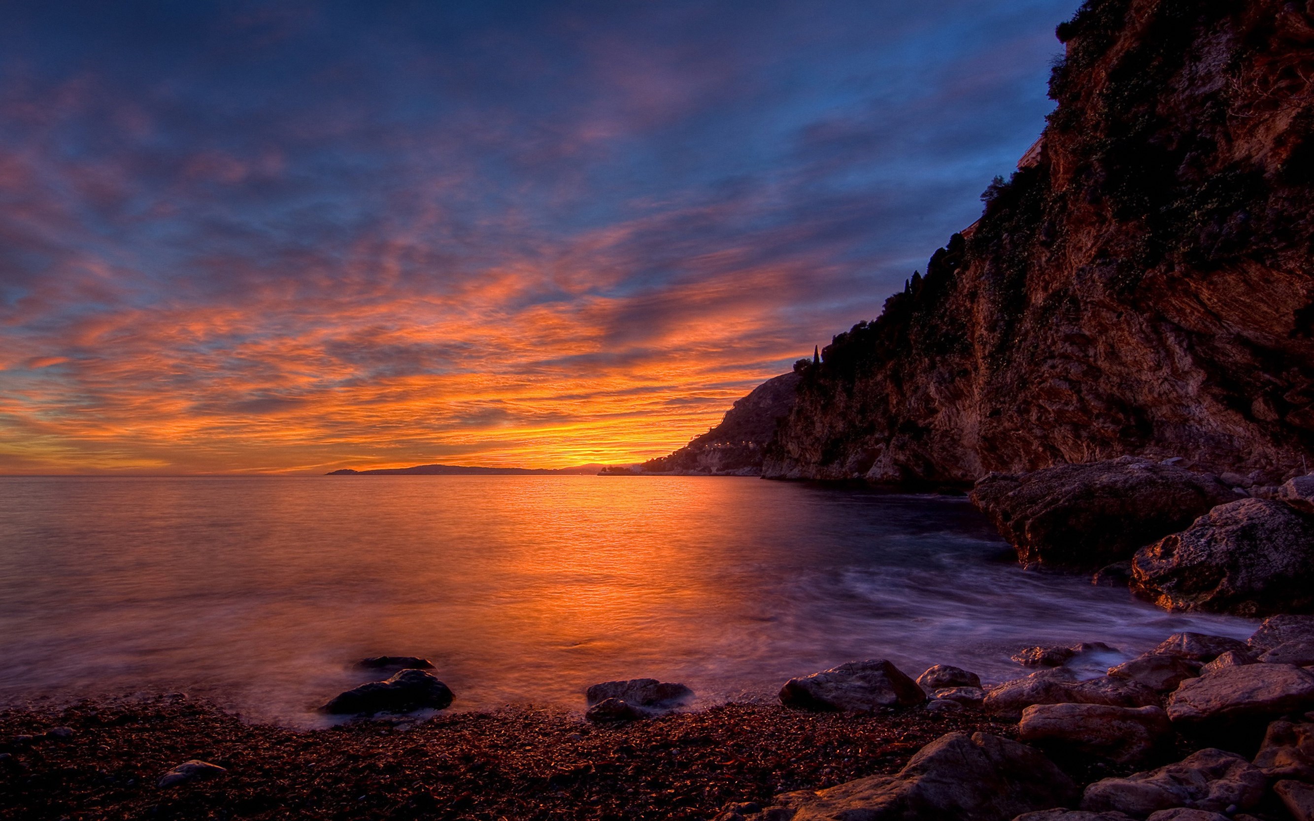 Sunset over a rocky coastline with calm water HD Wallpaper