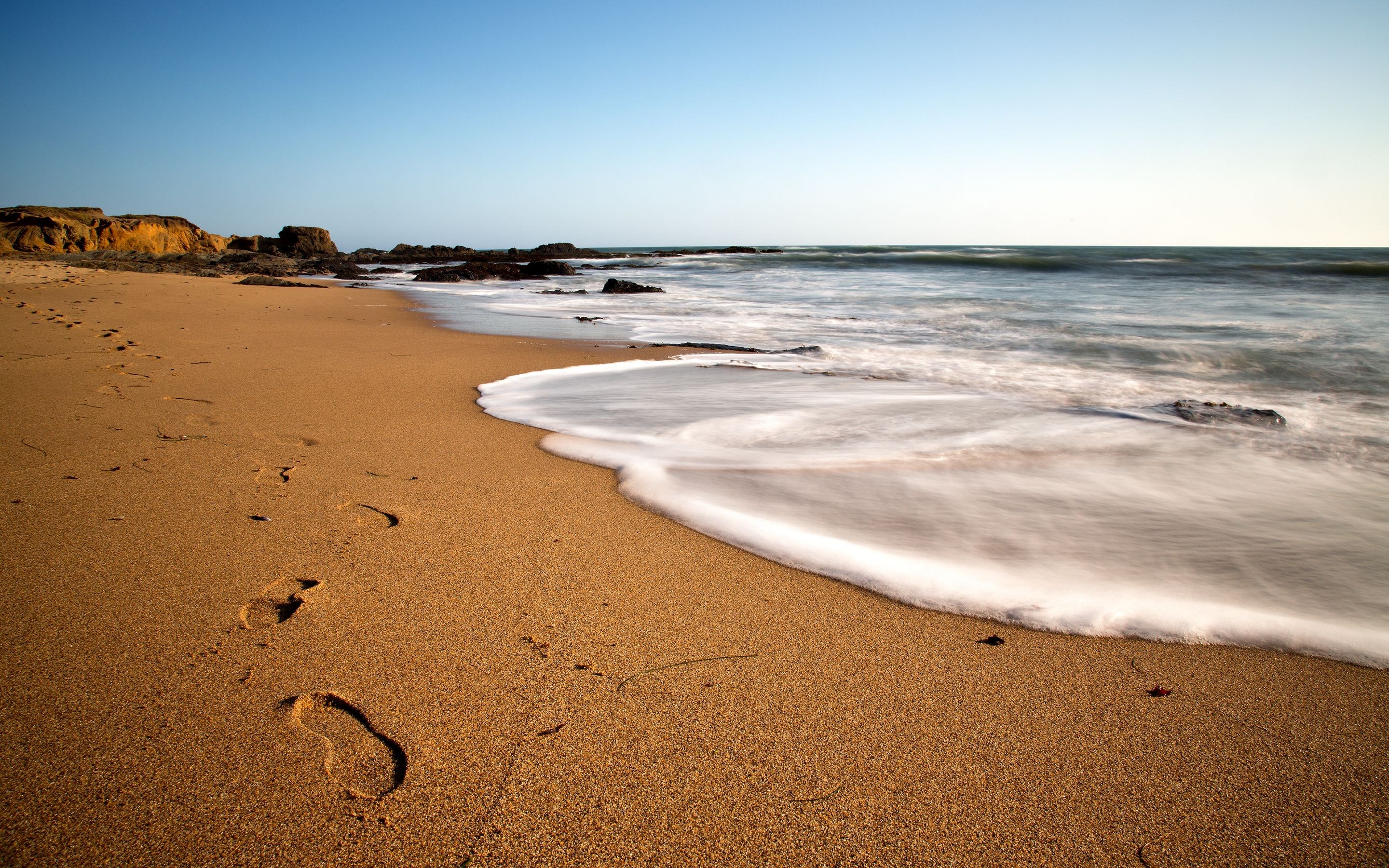 Footprints on a sandy beach with ocean waves HD Wallpaper