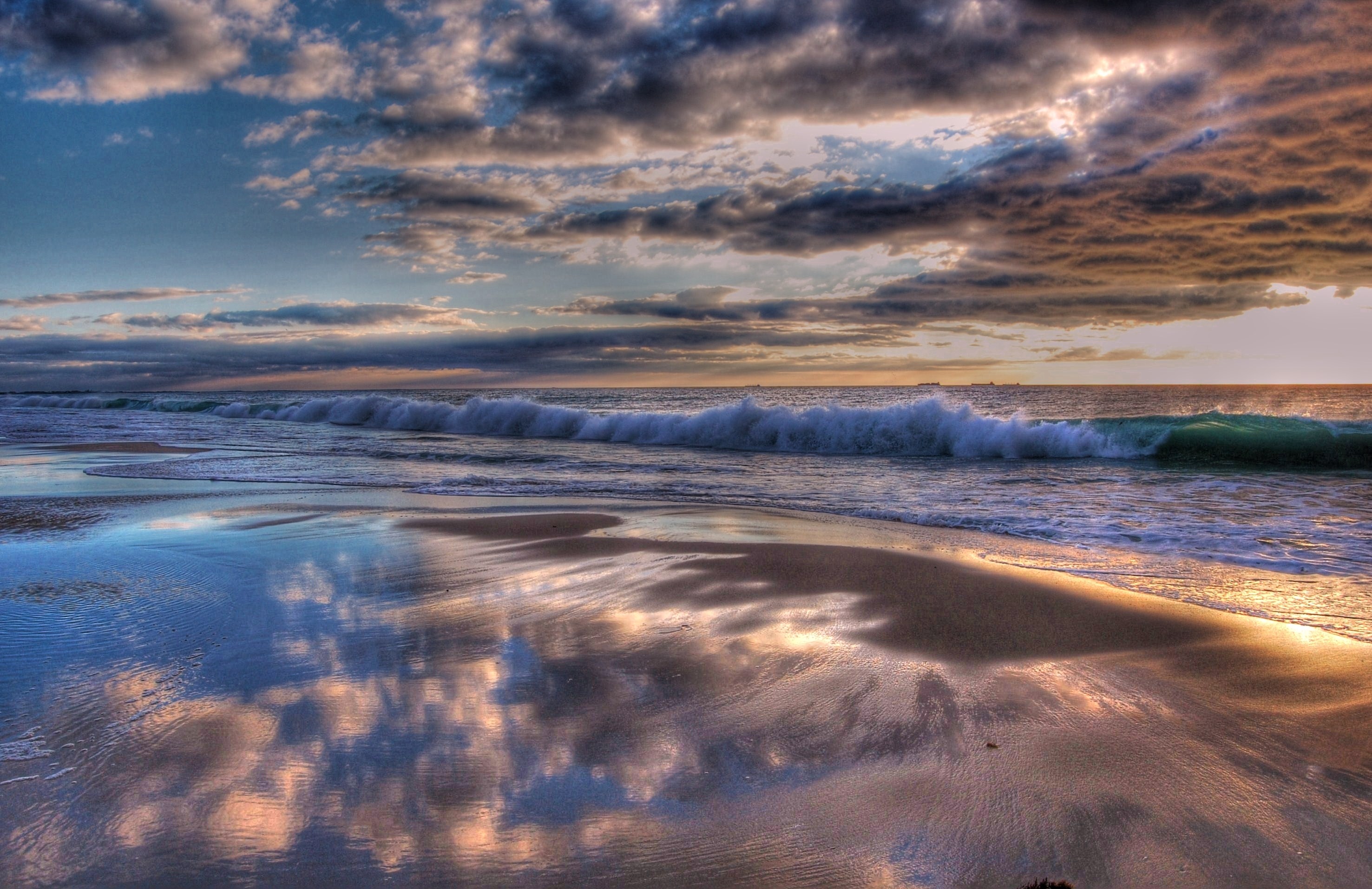 Ocean waves crashing on a sandy beach at sunset HD Wallpaper