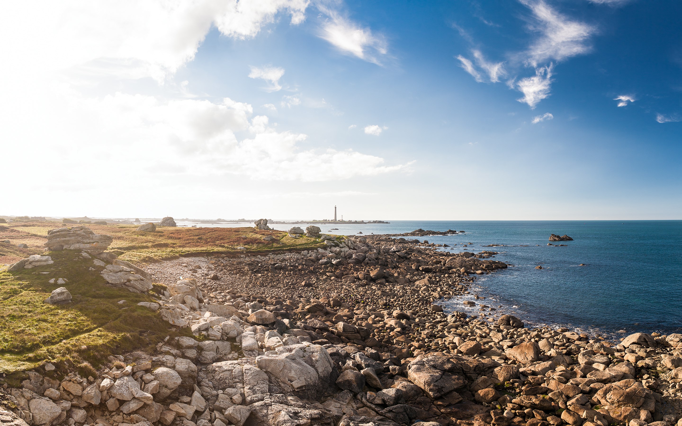 Rocky coastline with a lighthouse in the distance HD Wallpaper