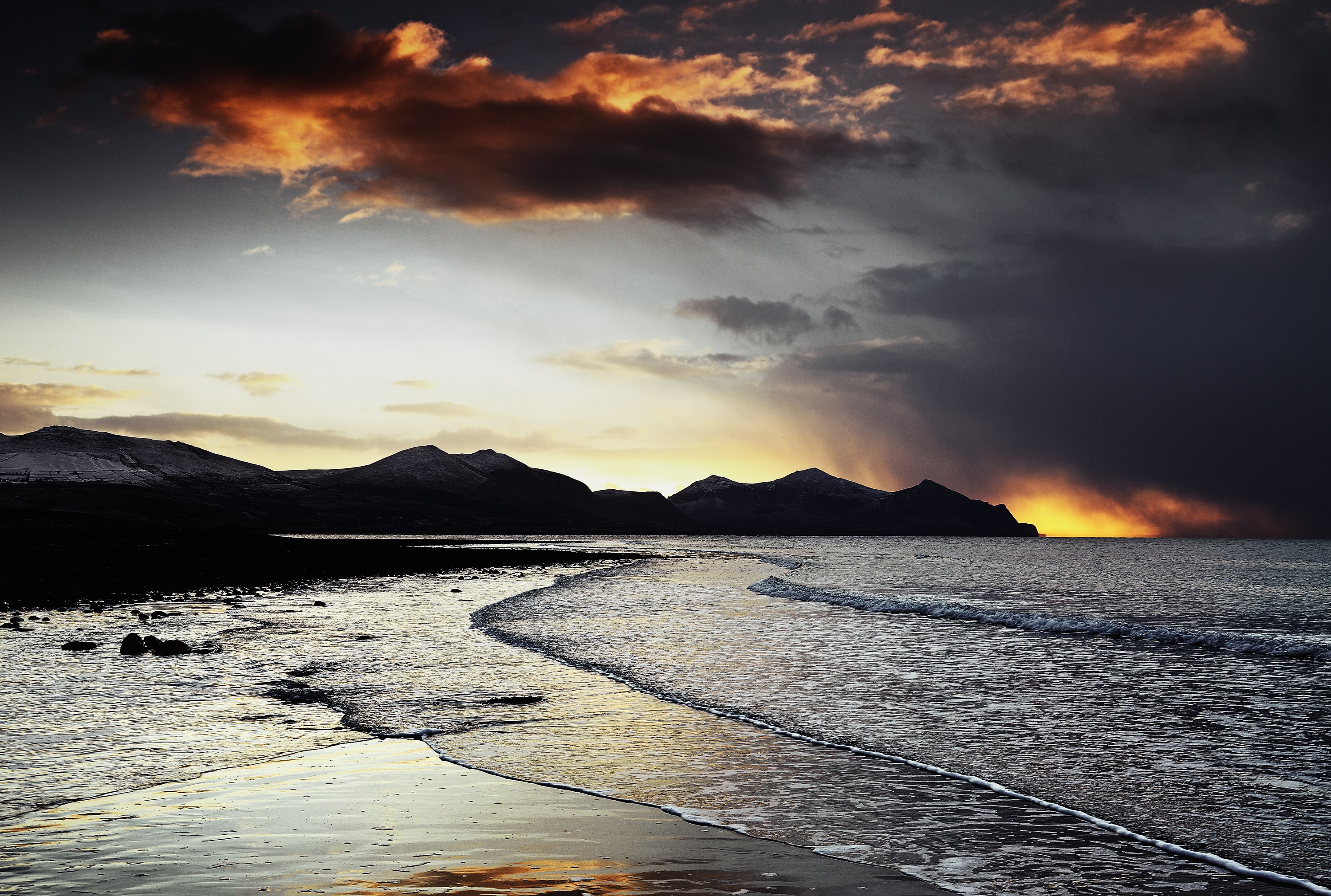 Dramatic sunset over a rocky beach and mountains HD Wallpaper