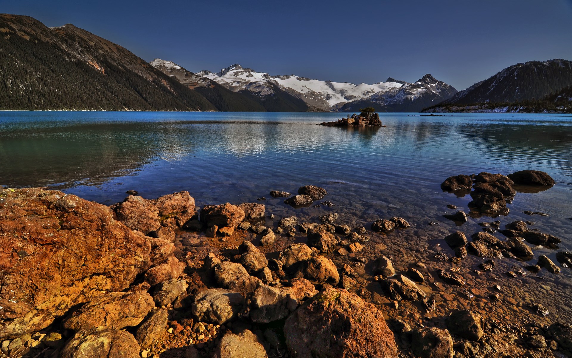 Rocky lake shore with snow-capped mountains HD Wallpaper