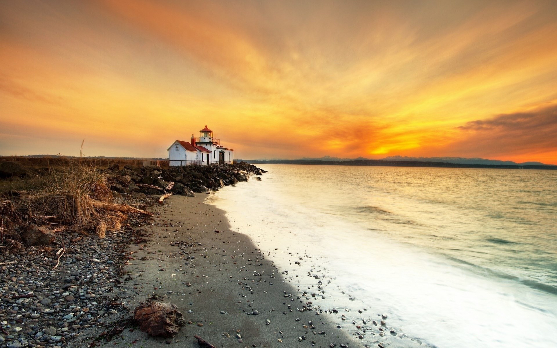 Lighthouse on a rocky shore during sunset HD Wallpaper