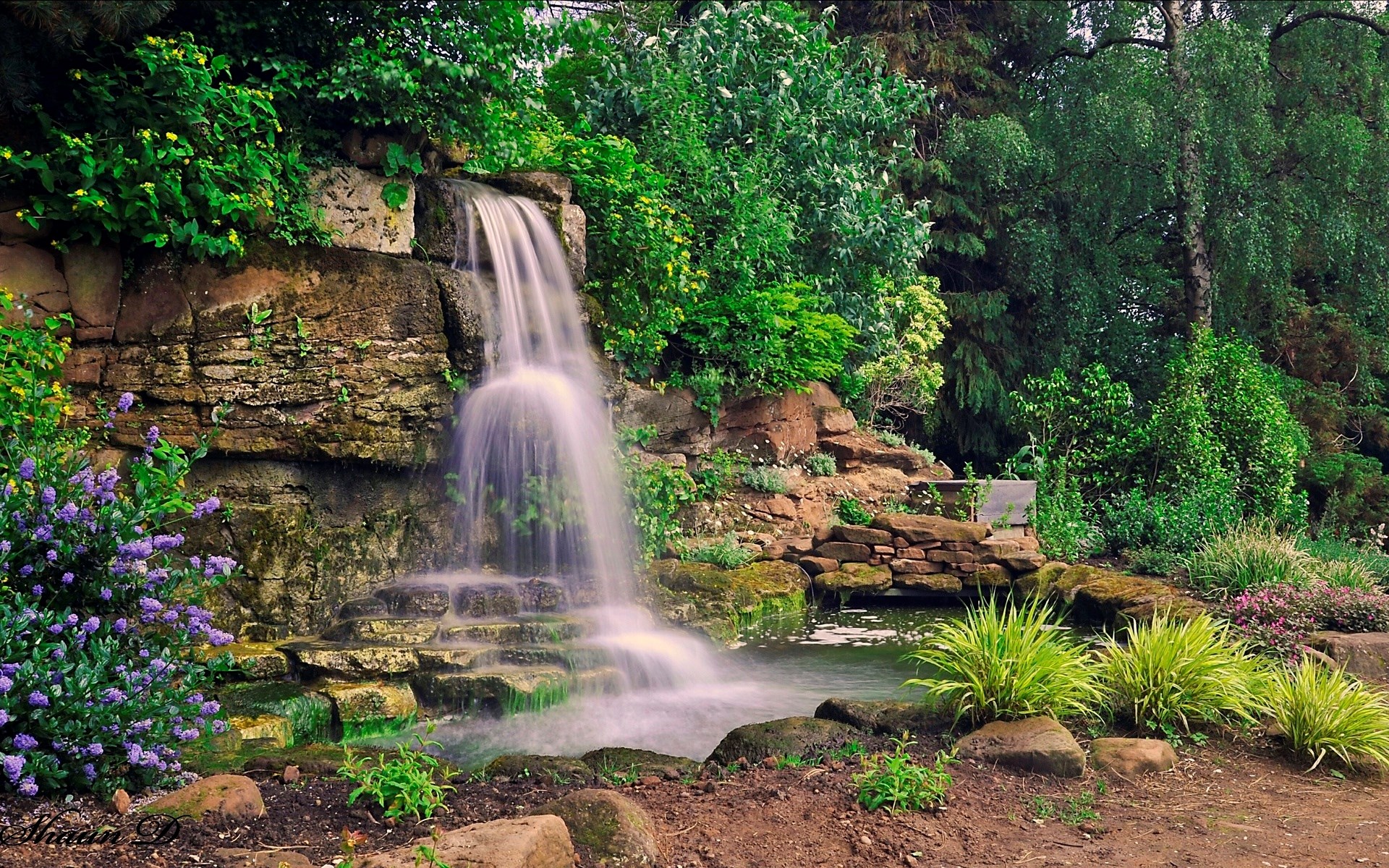 Waterfall cascading over rocks in a lush garden HD Wallpaper