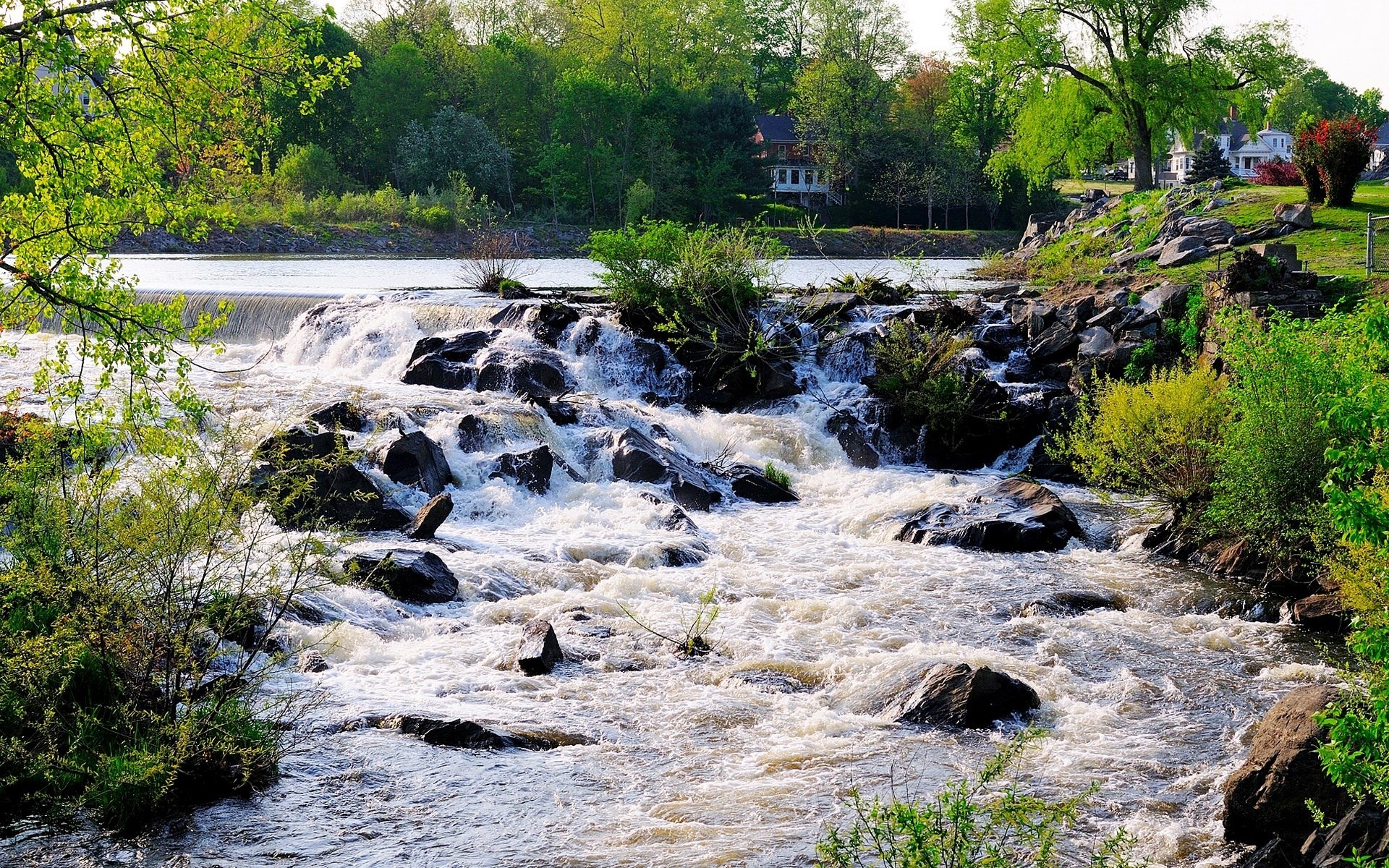 Waterfall cascading over rocks in a lush green landscape HD Wallpaper