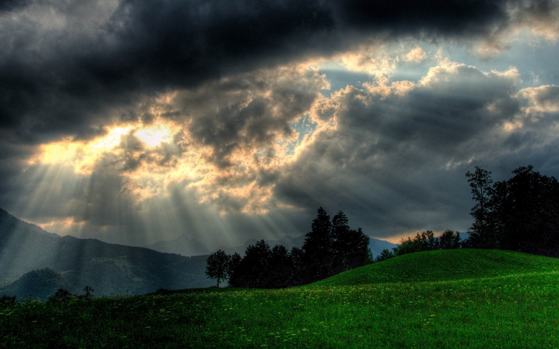 Sunbeams through storm clouds over mountains and a meadow HD Wallpaper