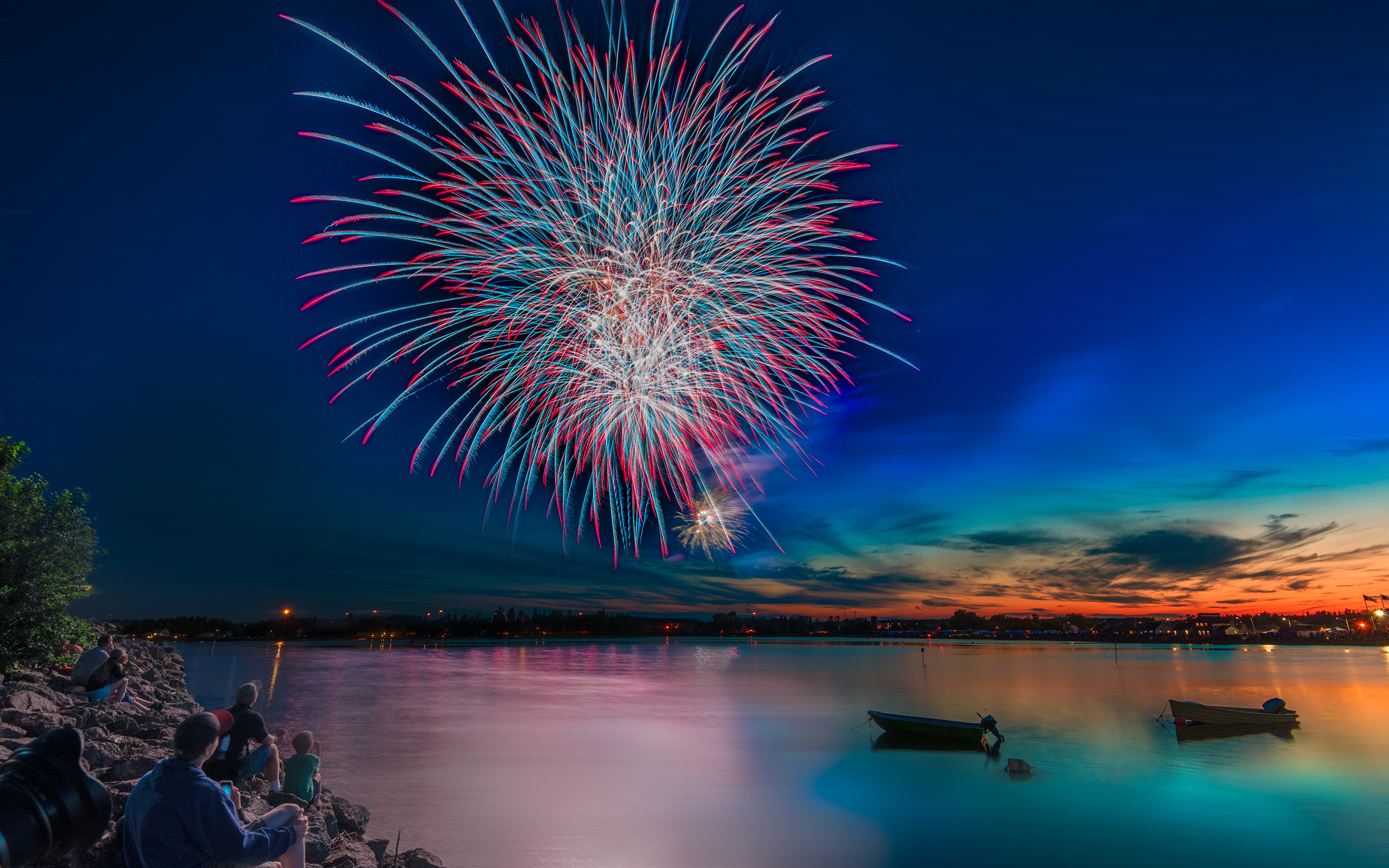 Fireworks over a lake at dusk with people watching HD Wallpaper
