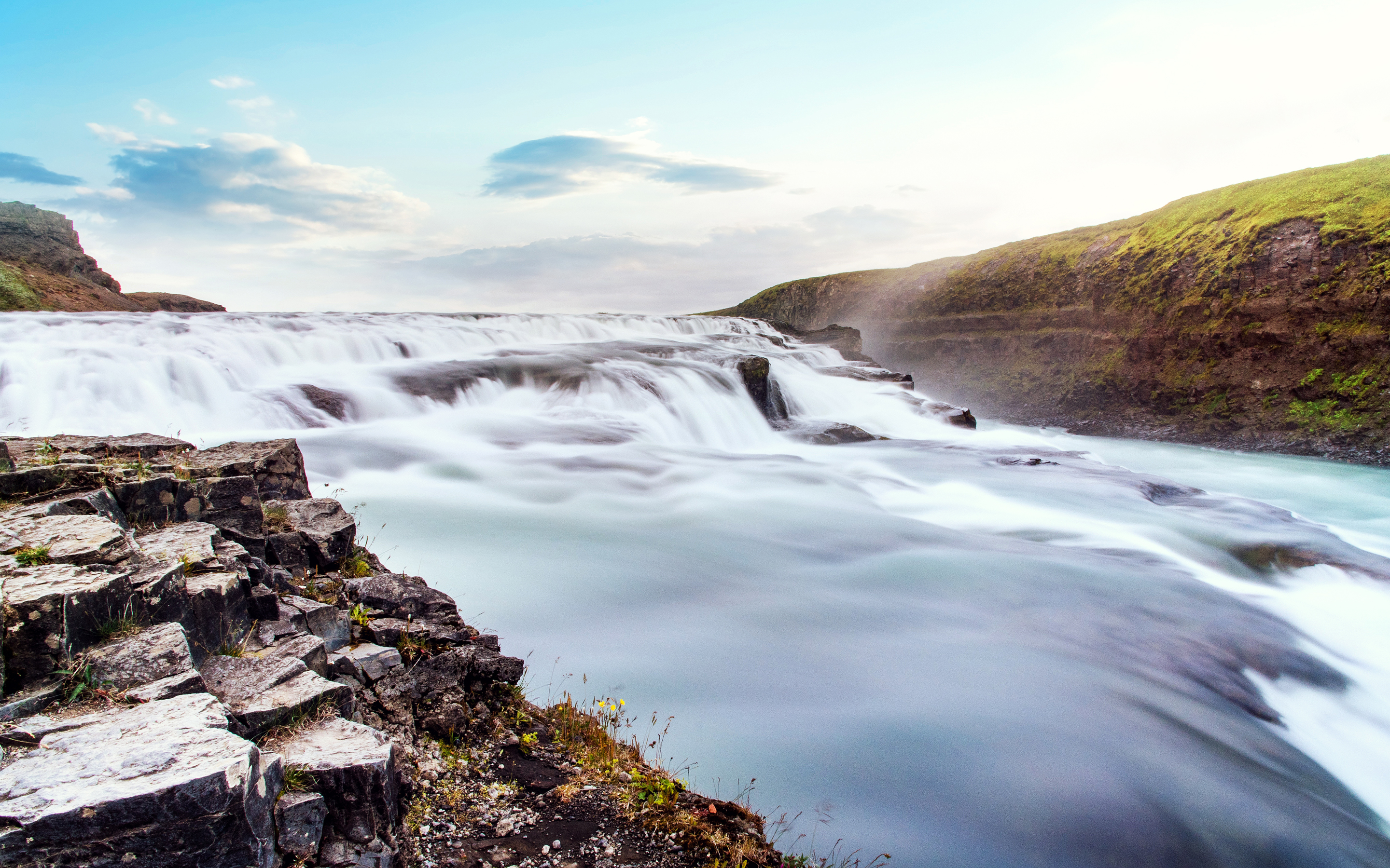 Wide waterfall cascading over rocks under a blue sky HD Wallpaper