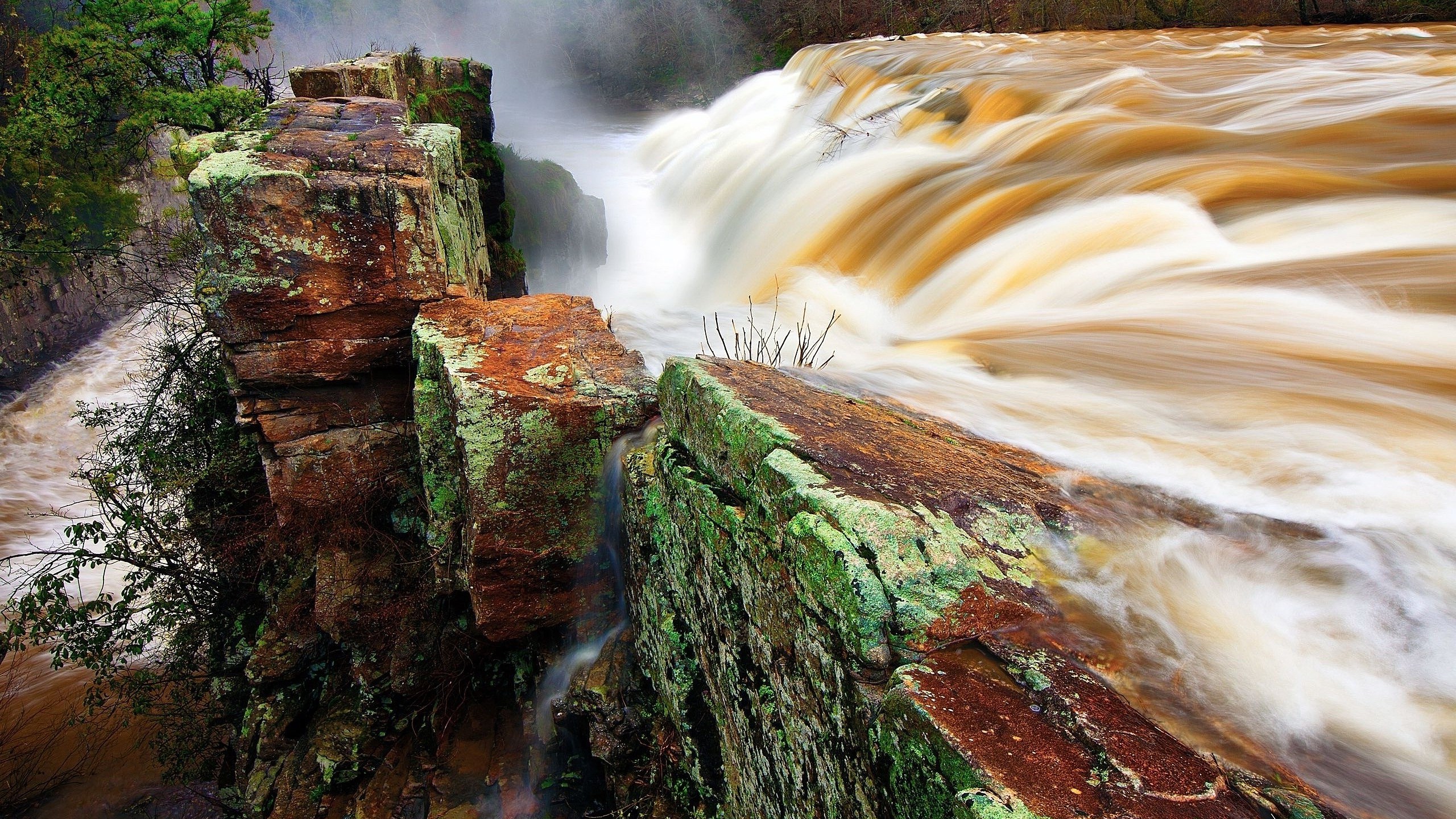 Brown waterfall cascading over mossy rocks HD Wallpaper