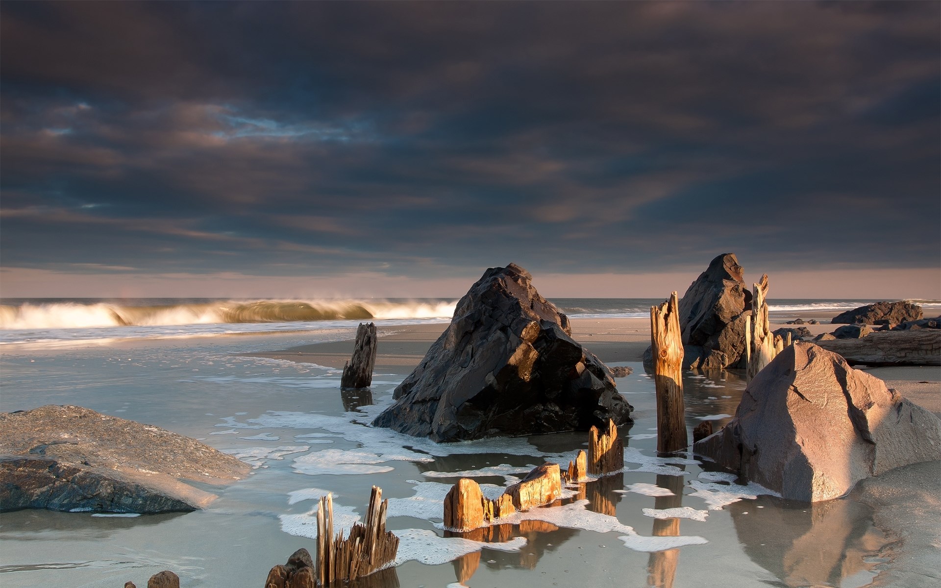 Rocky beach with waves and wooden posts at sunset HD Wallpaper