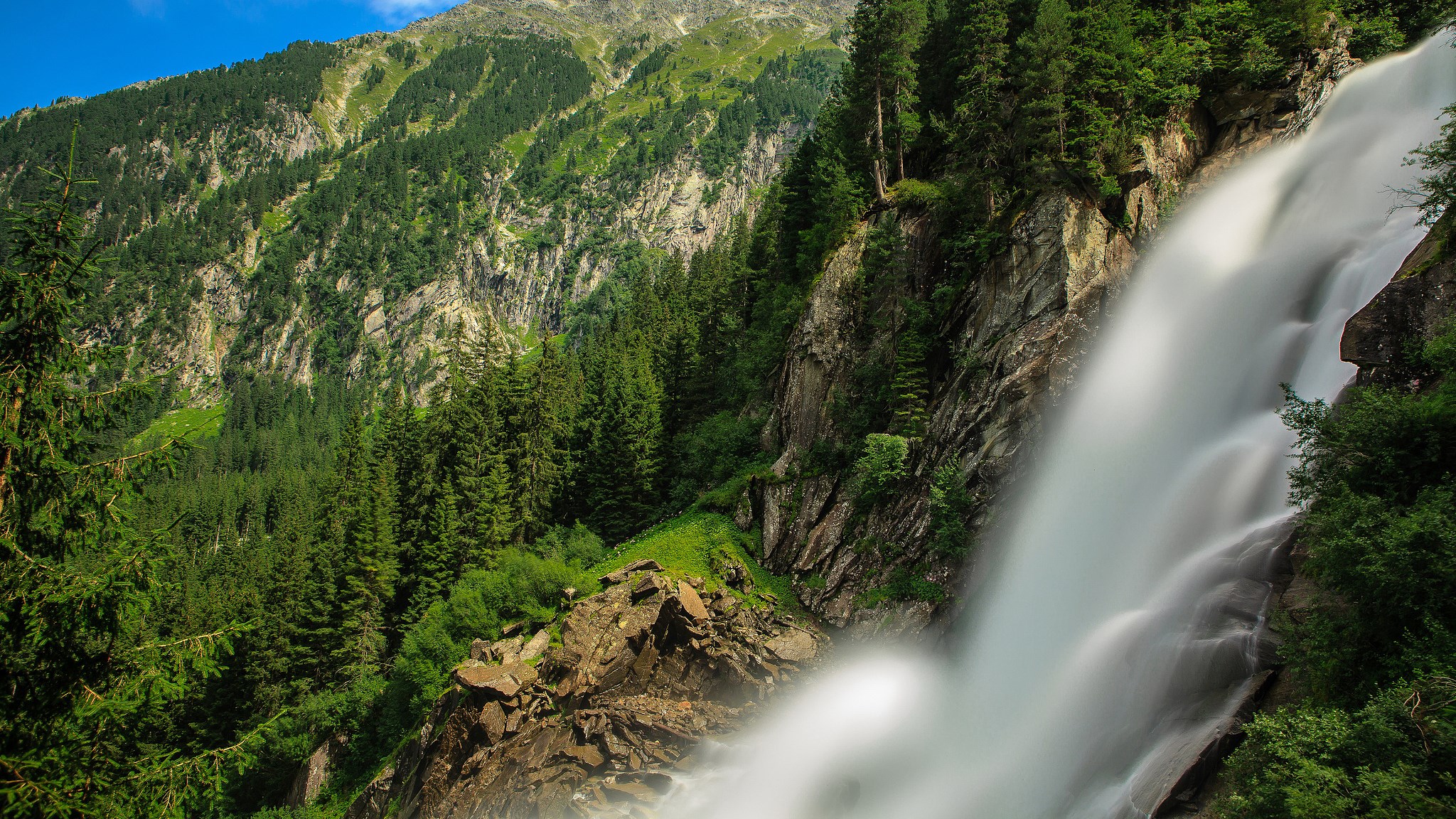 Waterfall cascading down a rocky mountain with pine trees HD Wallpaper