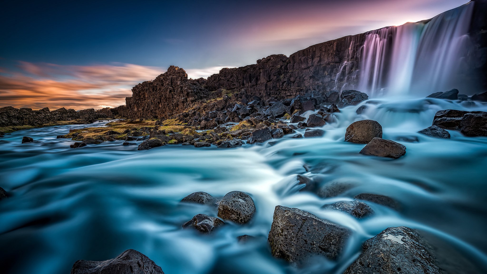 Waterfall flowing over rocks into a river HD Wallpaper