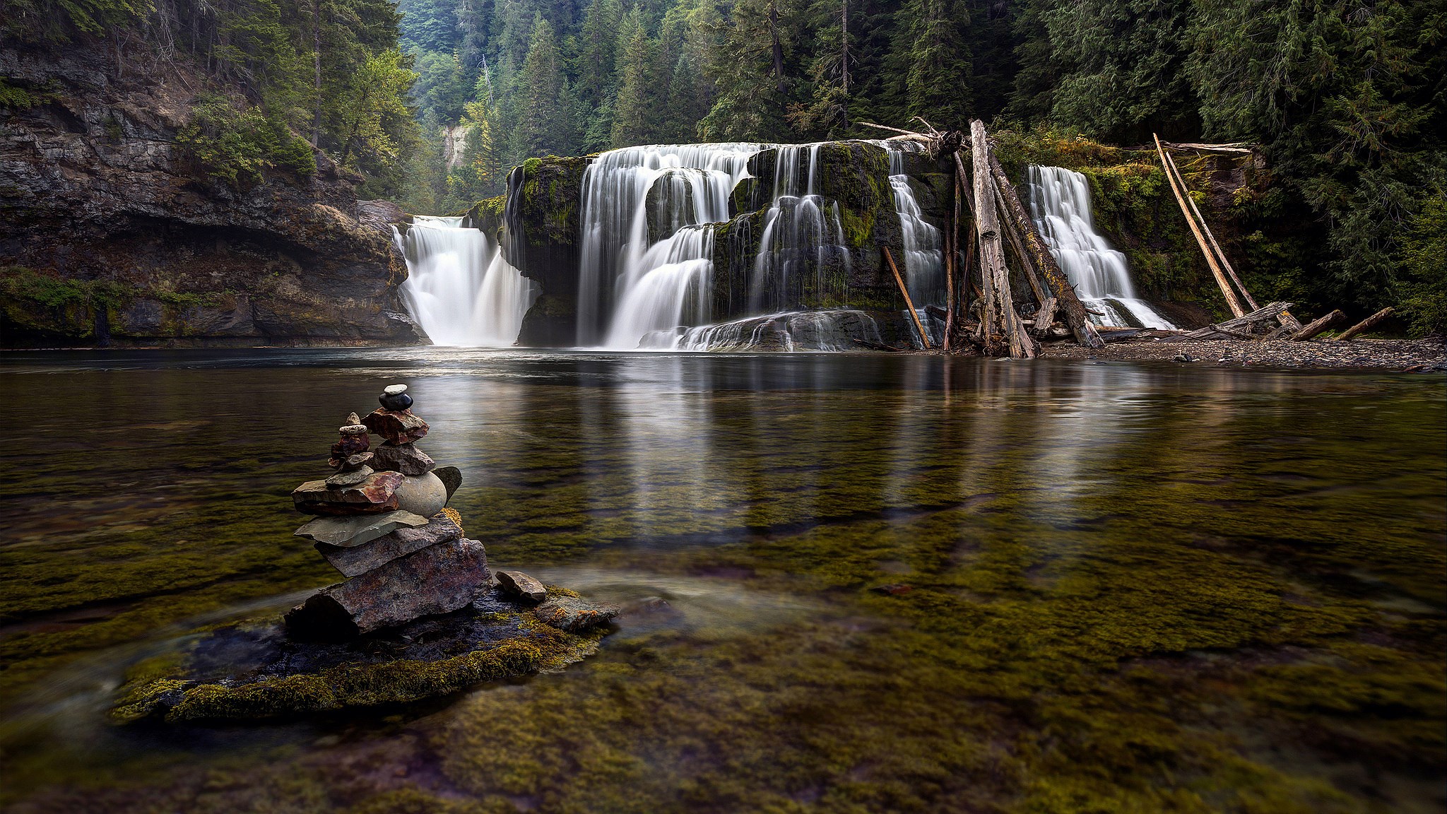 Waterfall cascading into a river with a stone cairn HD Wallpaper