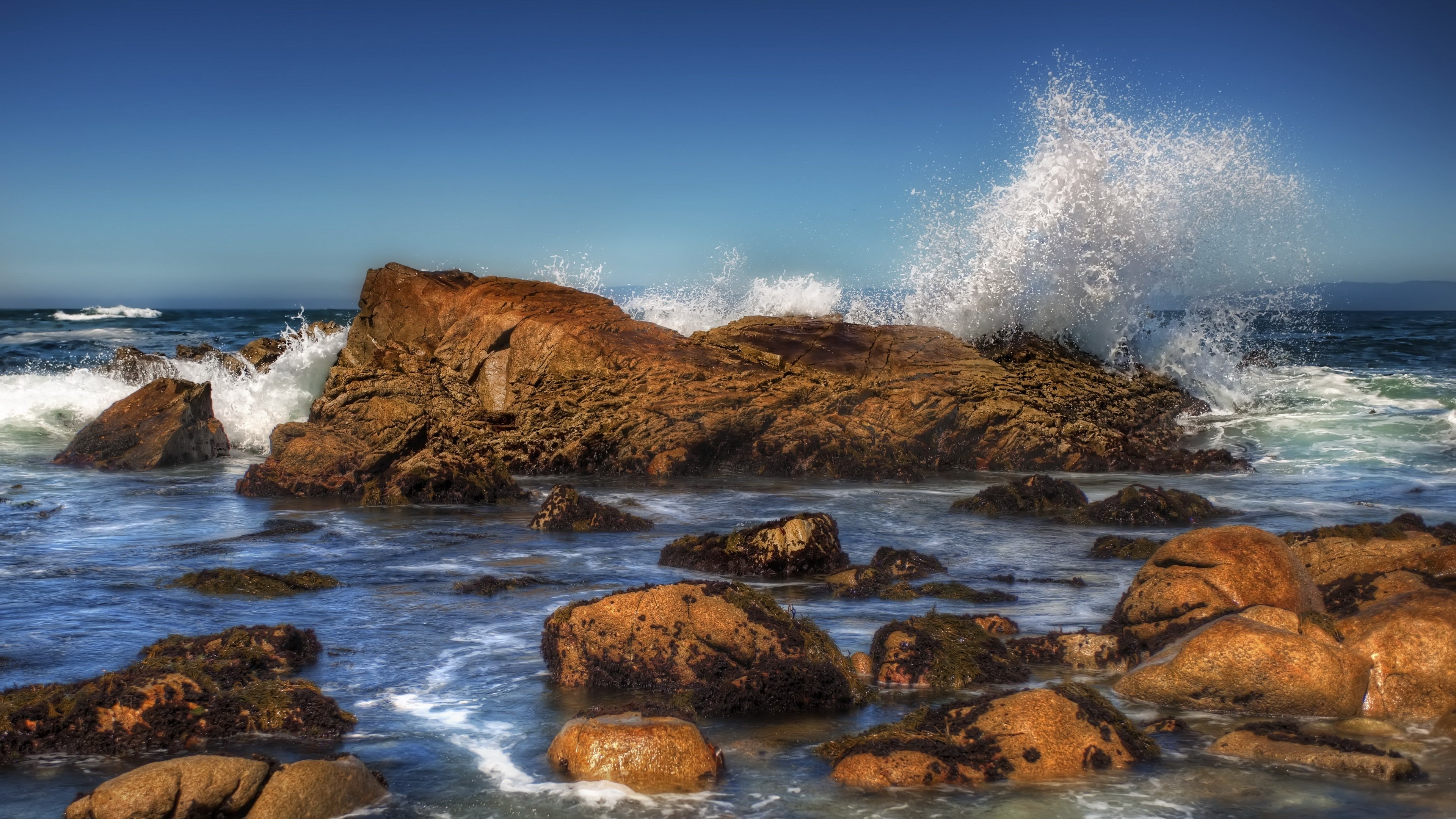 Waves crashing on rocky shore under blue sky HD Wallpaper