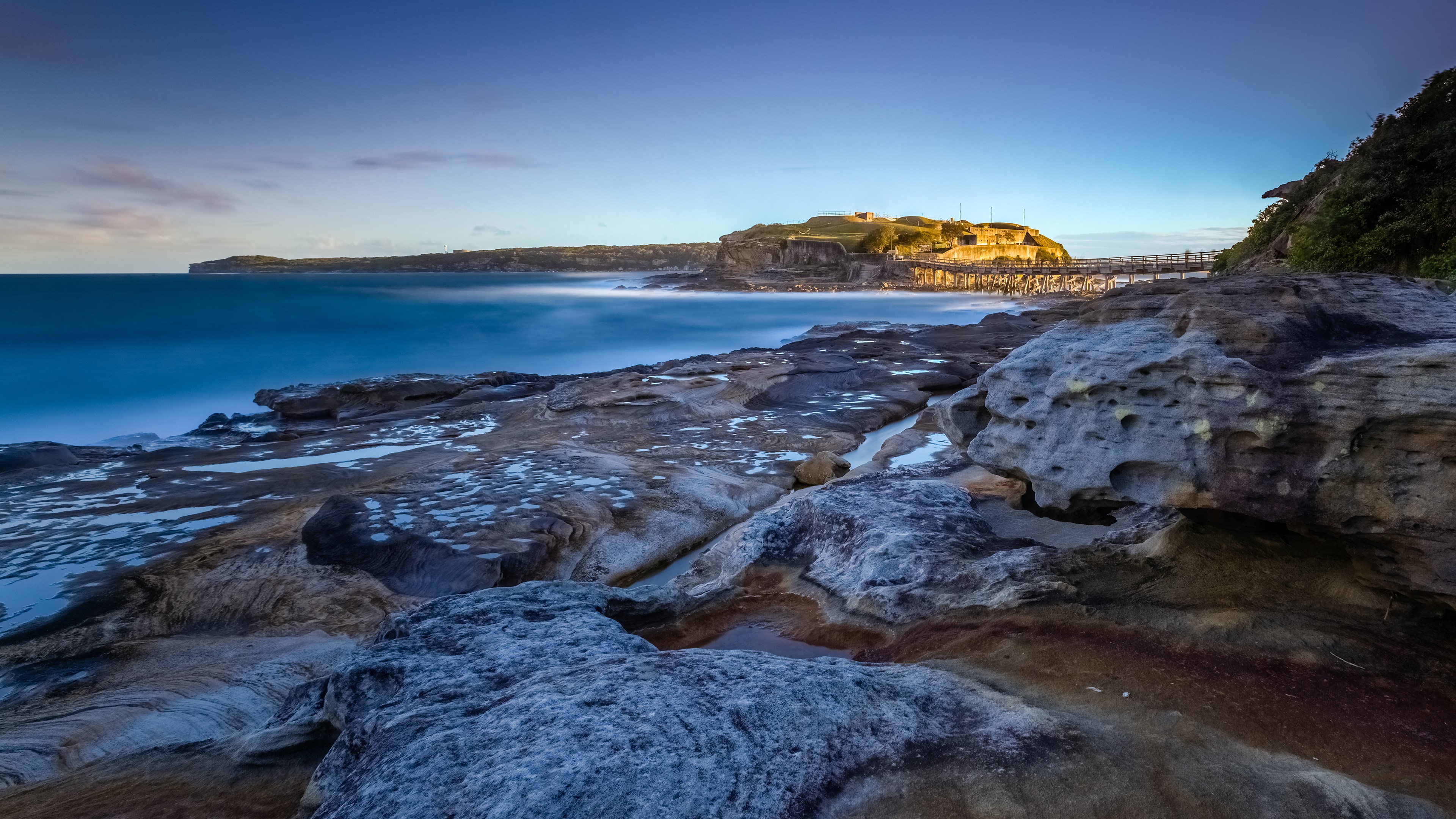 Rocky coastline with ocean and distant buildings HD Wallpaper