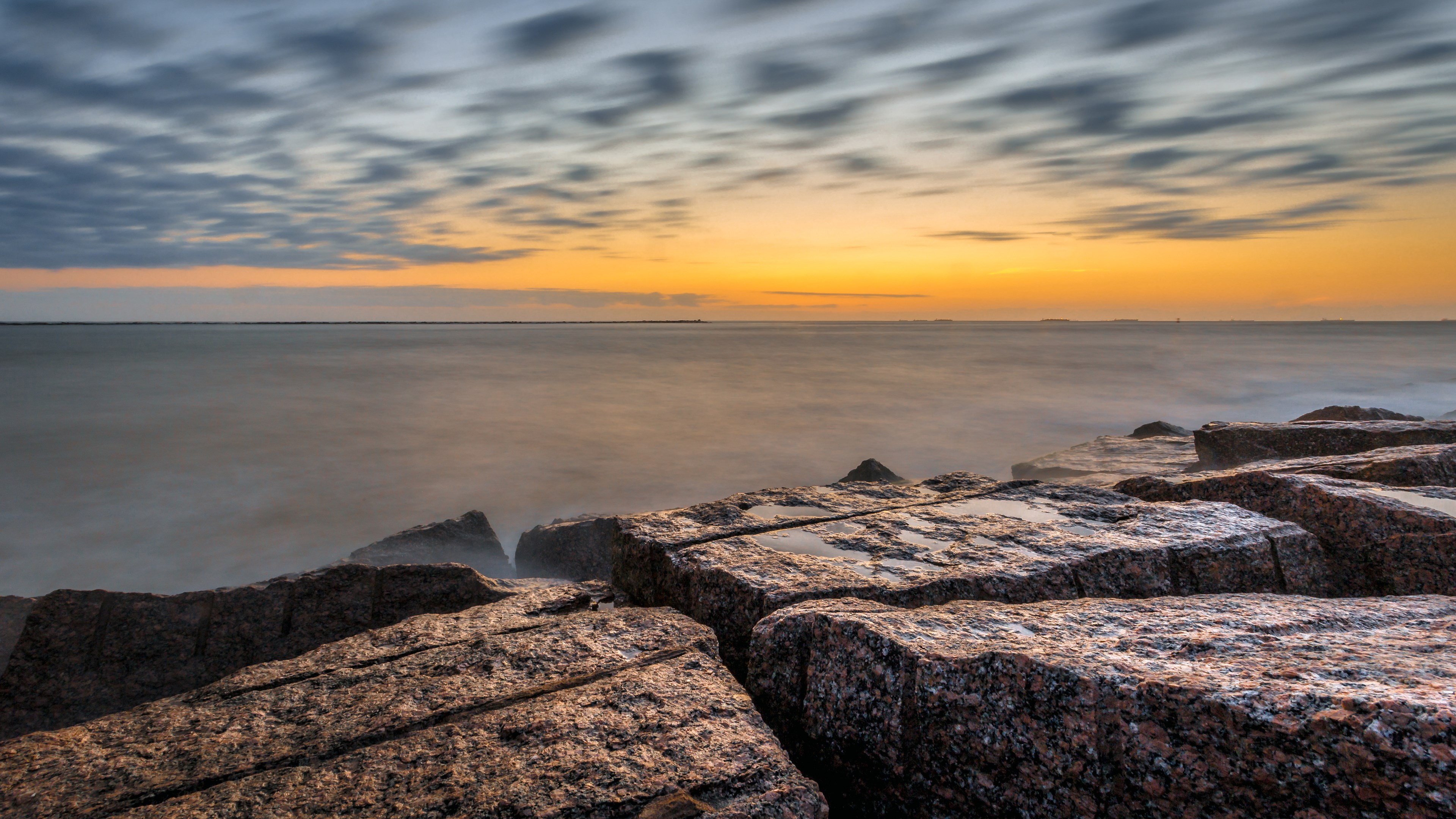 Rocky shore at sunset with blurred clouds HD Wallpaper