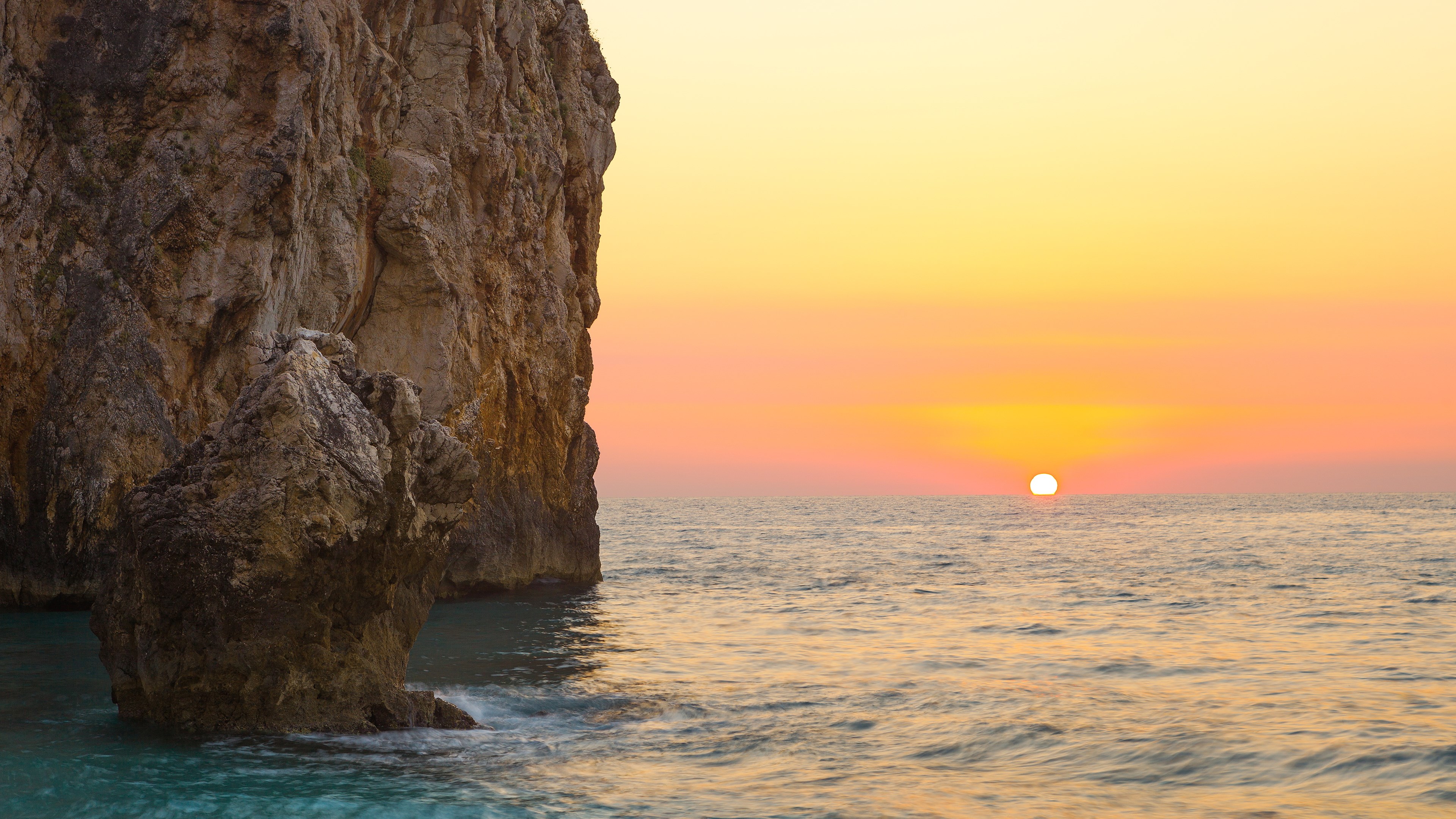 Sunset over the ocean with a rocky cliff HD Wallpaper