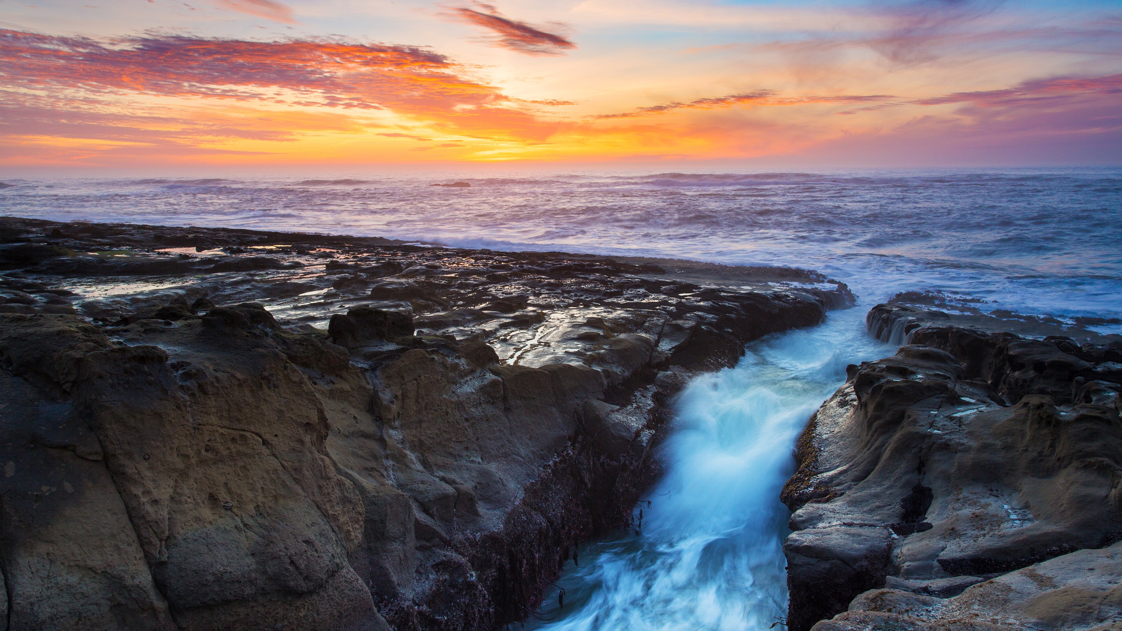 Ocean waves crashing on rocky shore at sunset HD Wallpaper
