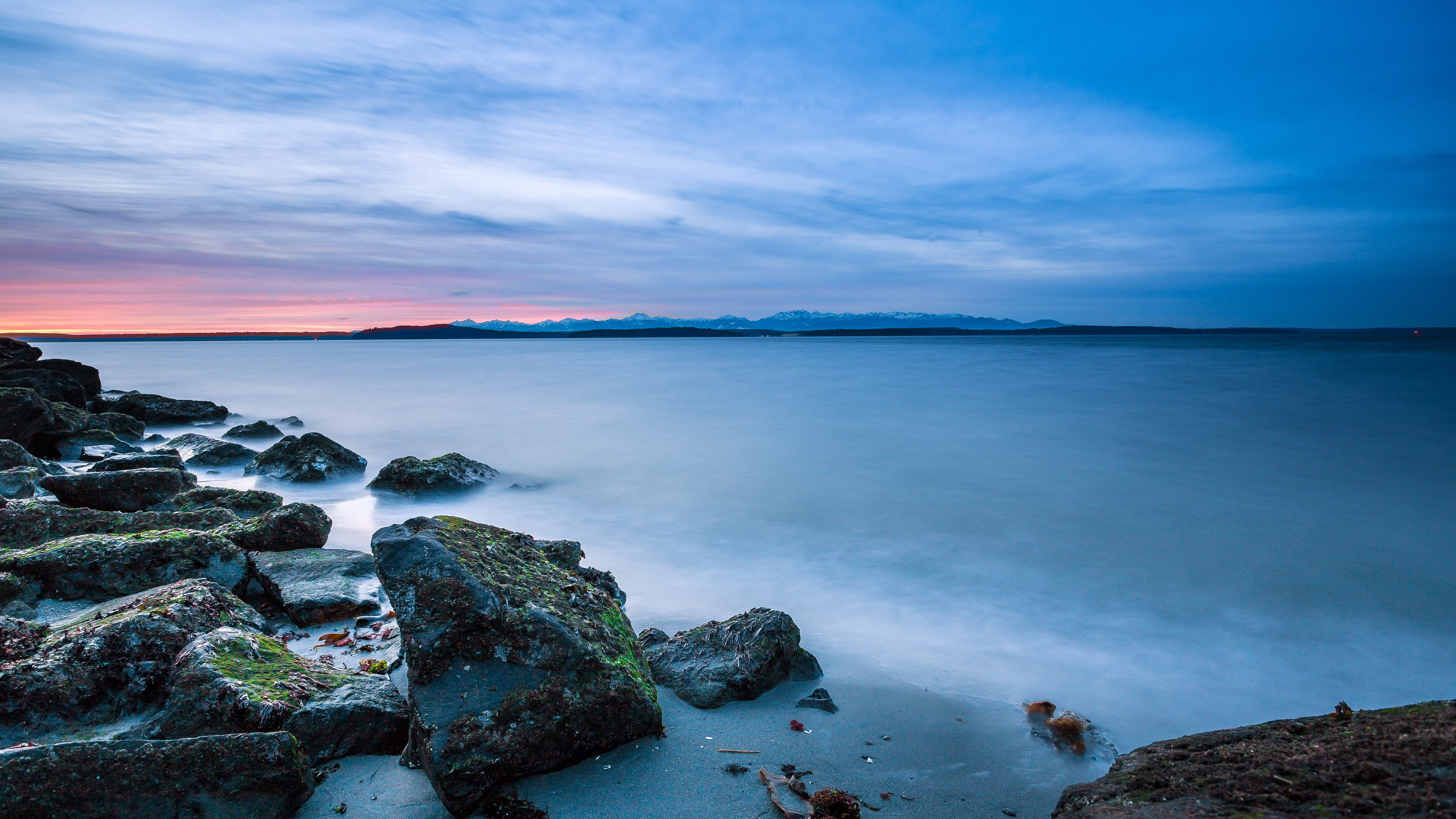 Ocean sunset with rocky shore and distant mountains HD Wallpaper