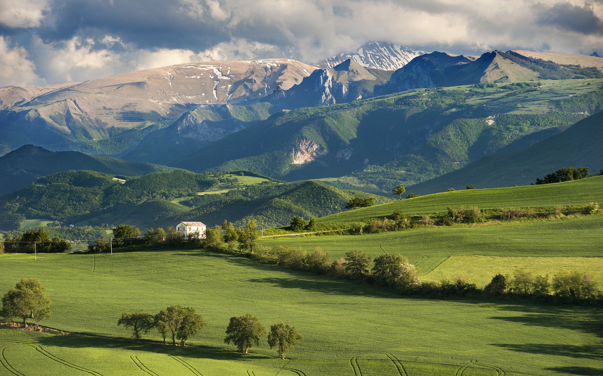 Green rolling hills and mountains with a white house HD Wallpaper