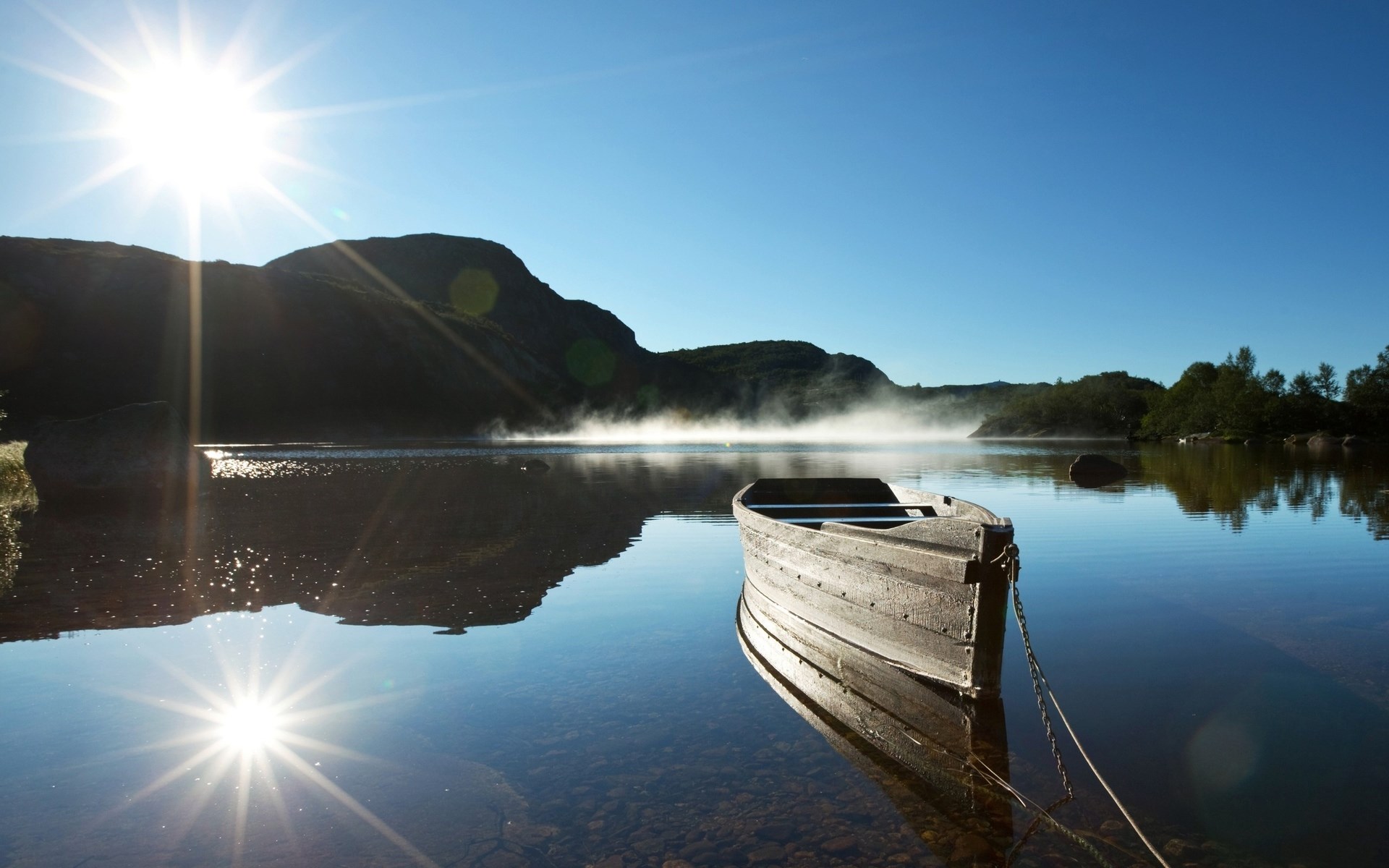 Wooden boat on a calm lake with mountains and sun HD Wallpaper